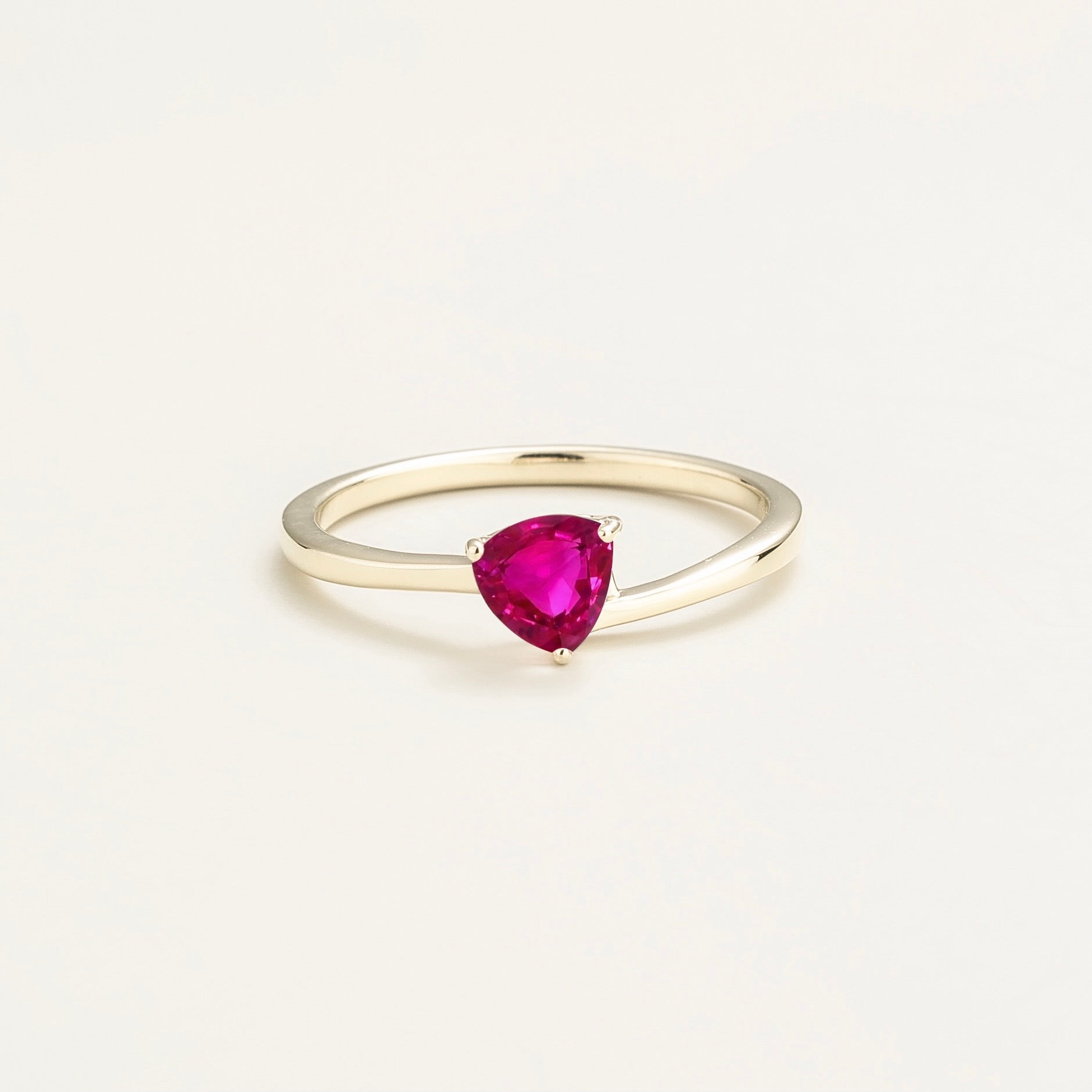 A solitaire white gold ring with a trillion-cut vivid pink sapphire in a curved modern setting on a plain background.