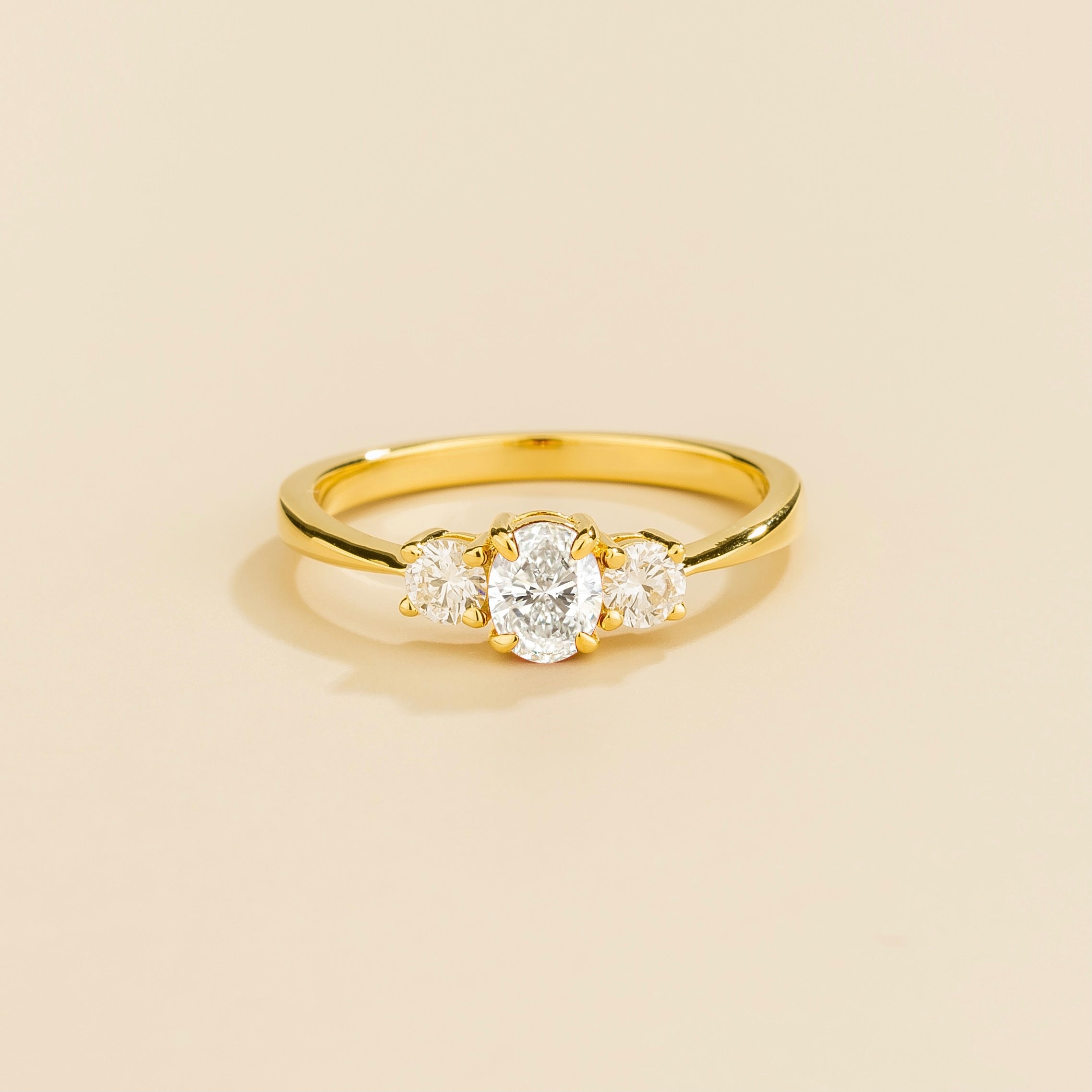 3 gemstones gold ring featuring a central diamond with two smaller diamonds on either side, set against a plain background.