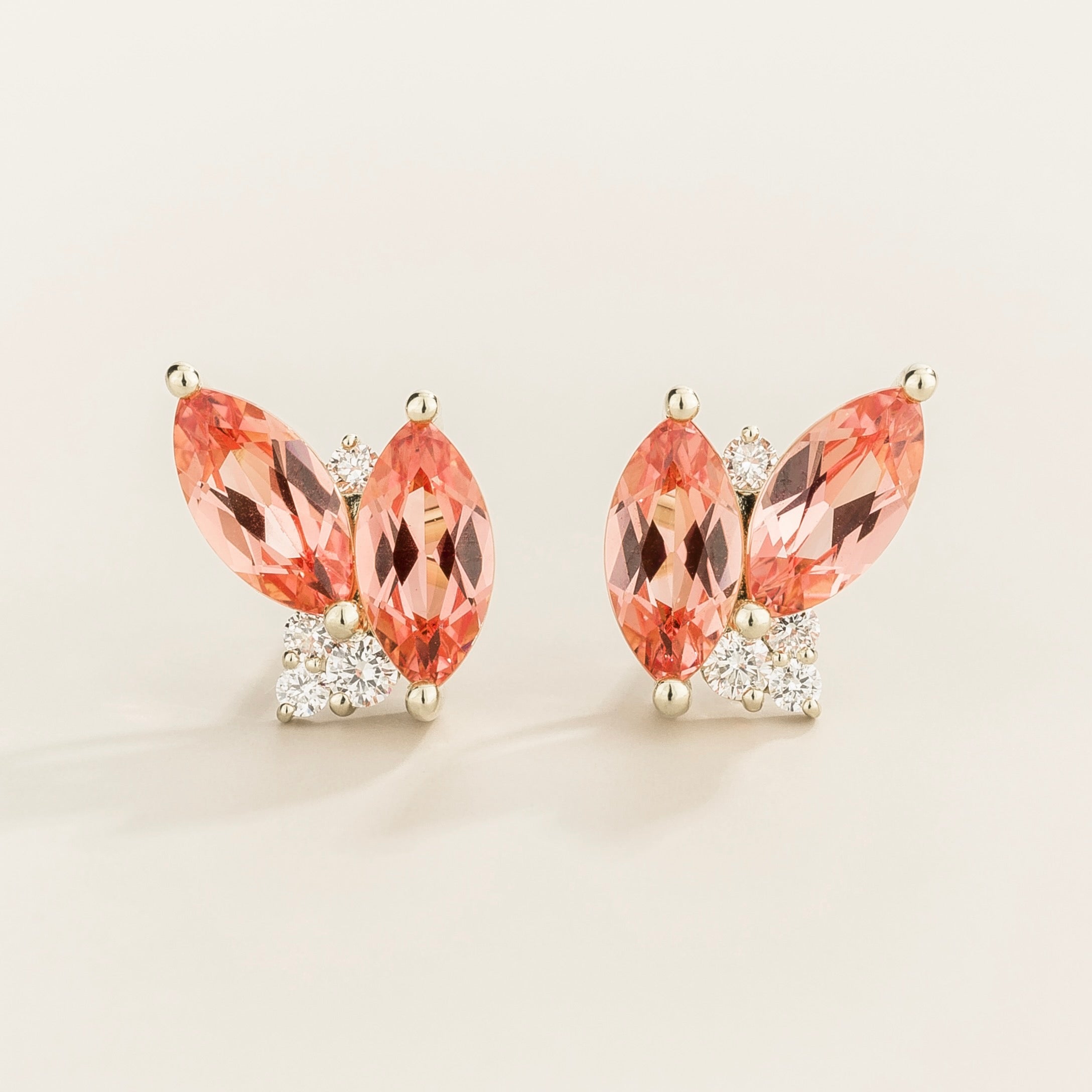 Pair of earrings with marquis padparadscha sapphire gemstones and white gold with diamond accents on a light background