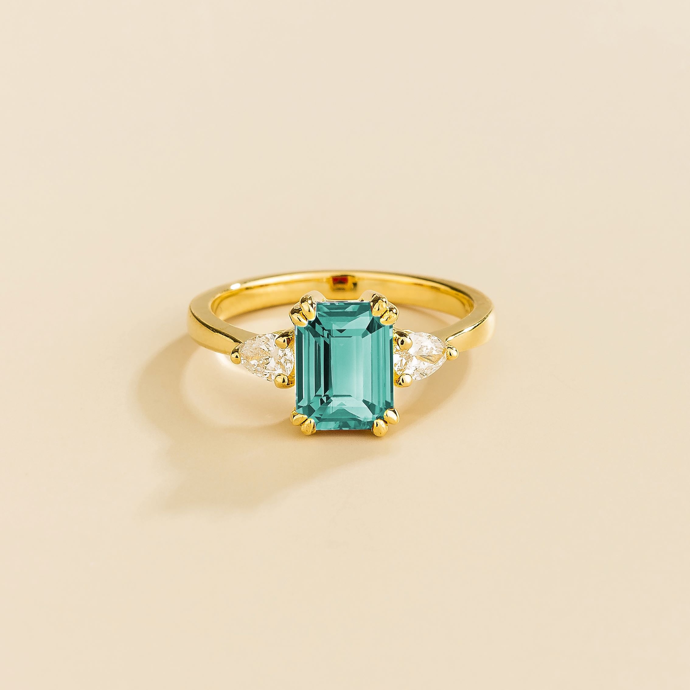 A ring with a paraiba sapphire center stone and pear shape diamonds set in yellow gold, emerald/octagon cut for the sapphire.
