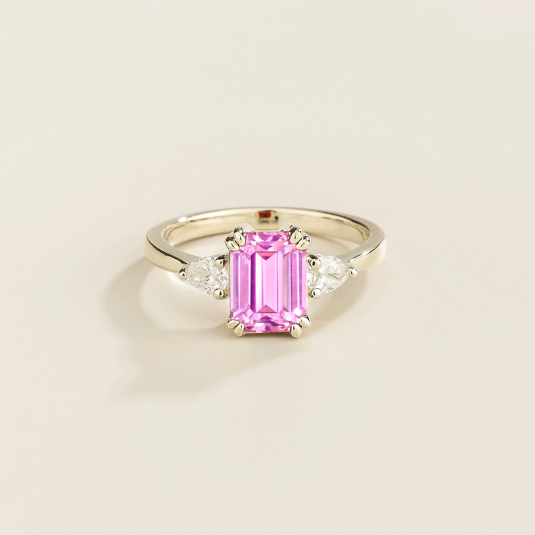 A ring with a pink sapphire center stone and pear shape diamonds set in white gold, emerald/octagon cut for the sapphire.