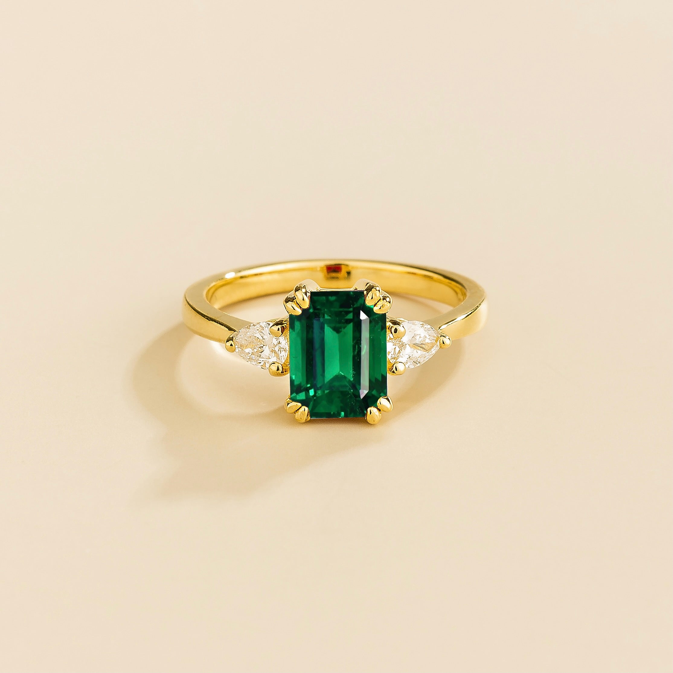 A gold ring with a emerald cut gemstone and smaller pear shape diamonds on the side
