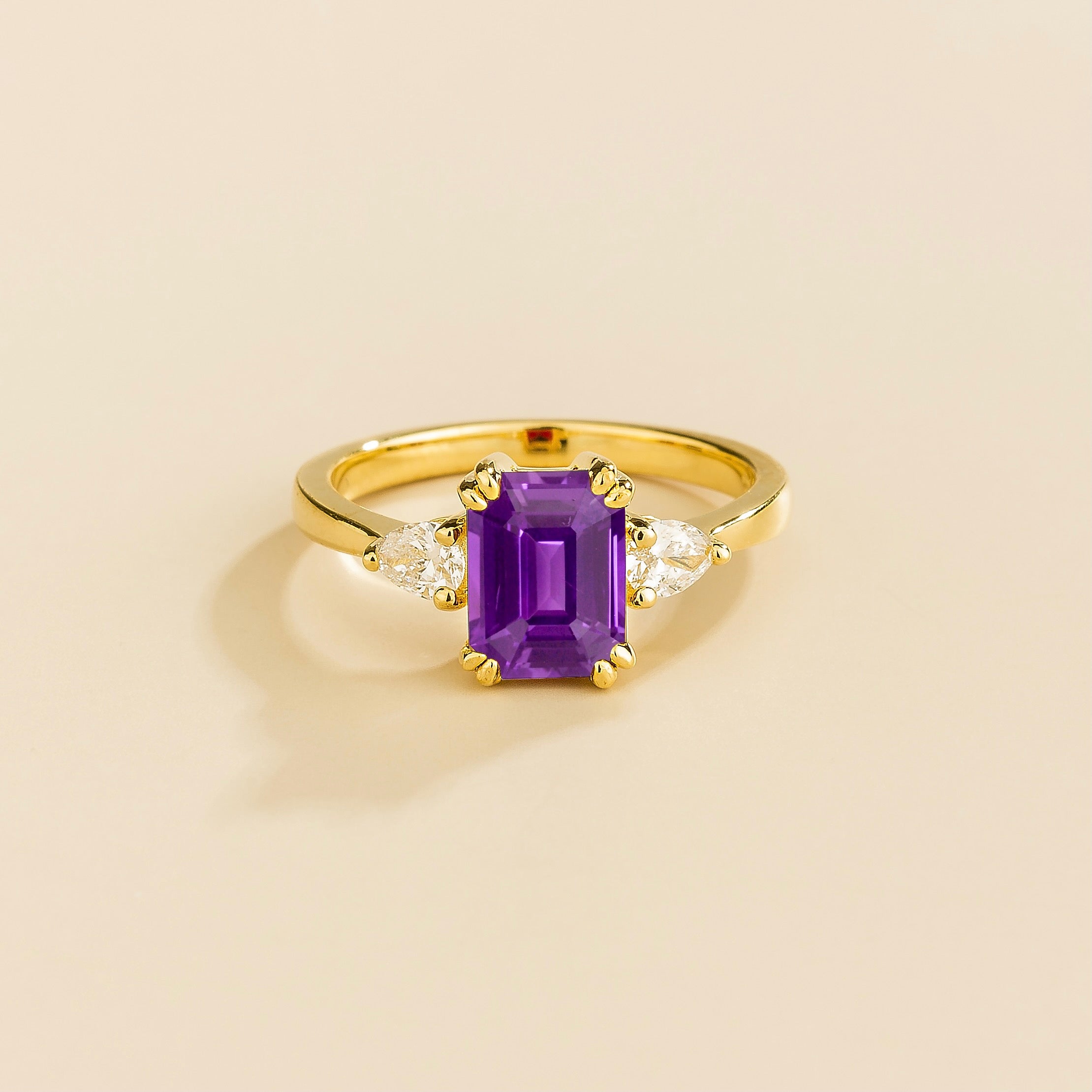 A ring with a purple sapphire center stone and pear shape diamonds set in yellow gold, emerald/octagon cut for the sapphire.