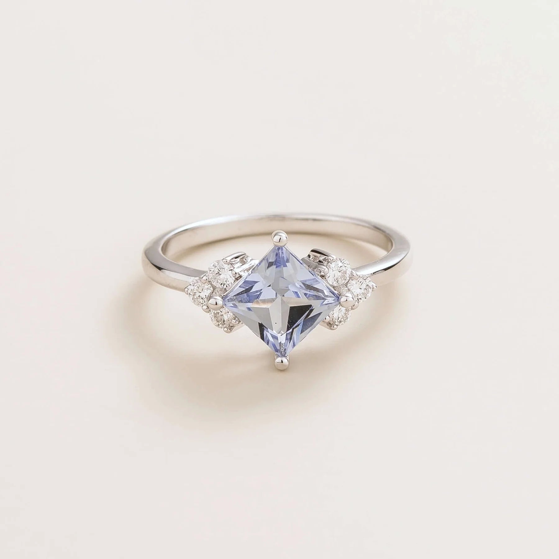A white gold ring with a princess cut pastel blue sapphire center stone and smaller diamonds set around.