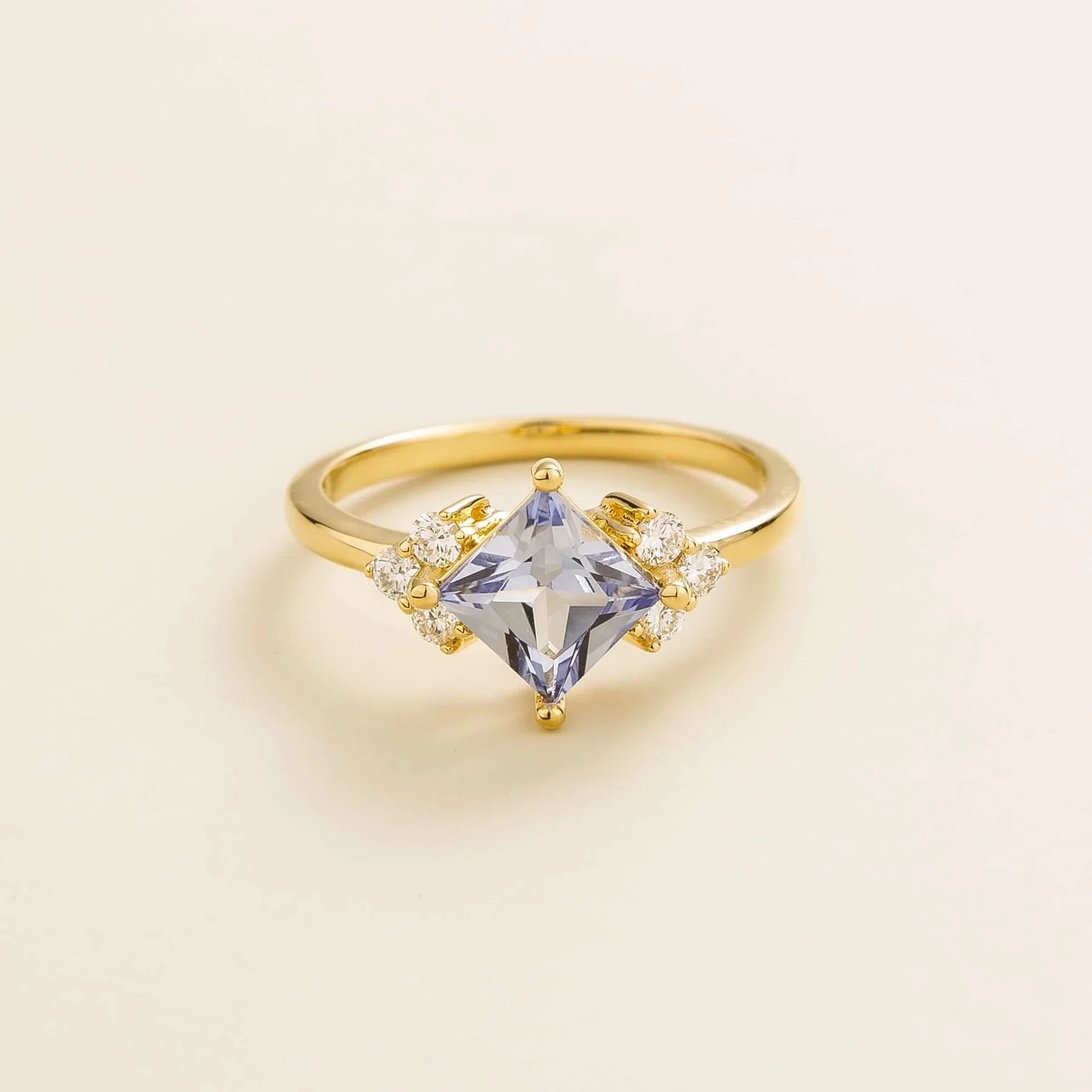 A gold ring with a princess cut pastel blue sapphire center stone and smaller diamonds set around.London