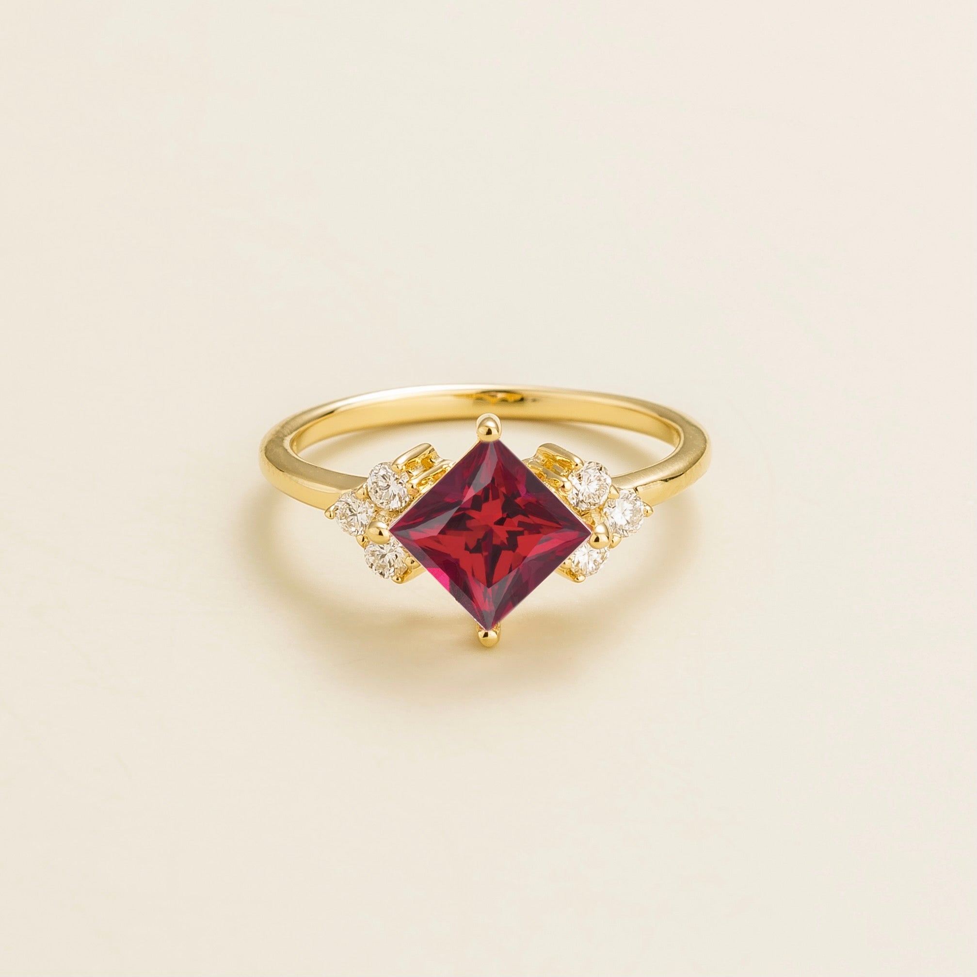 A gold ring featuring a princess cut ruby center stone with smaller diamond accents on the sides.