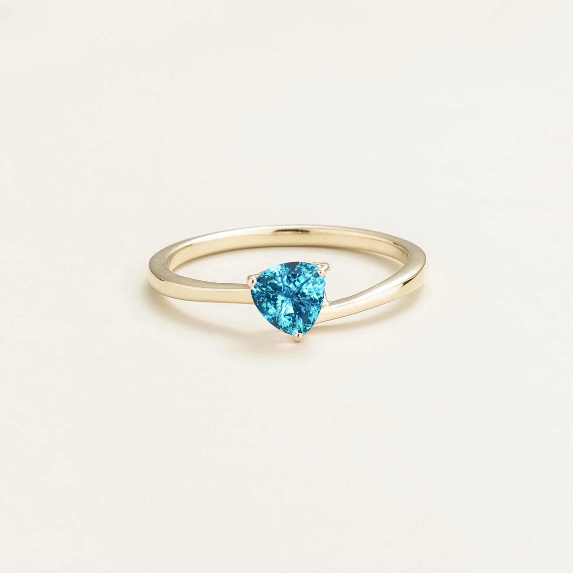A solitaire white gold ring with a trillion-cut paraiba in a curved modern setting on a plain background.