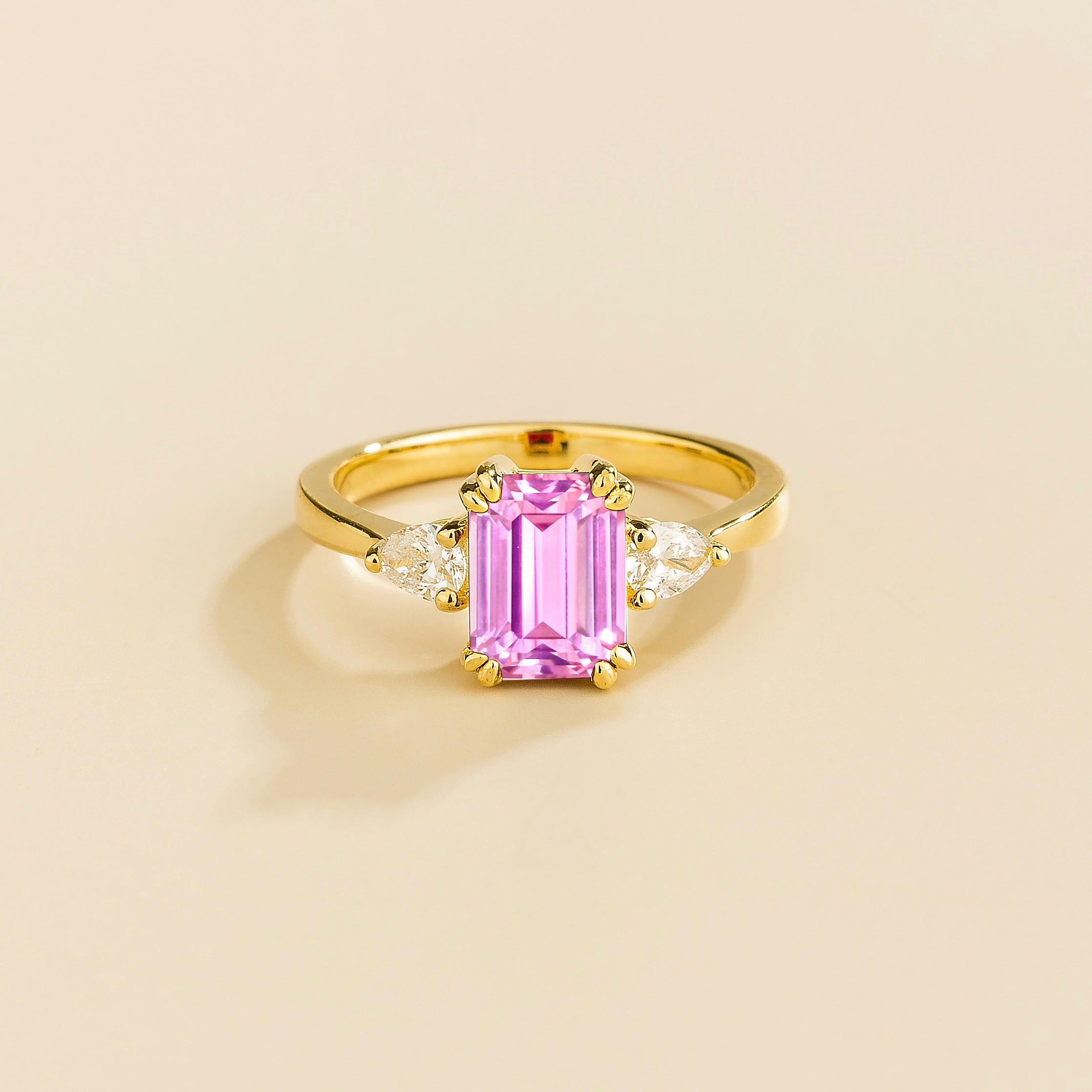A gold ring with a pink sapphire center stone and pear shape diamonds set in yellow gold, emerald/octagon cut for the sapphire.