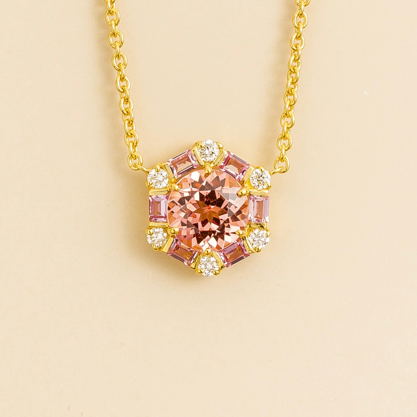 A gold necklace set with a central padparadscha sapphire pendant, surrounded by pink sapphires and diamonds, on a plain background.