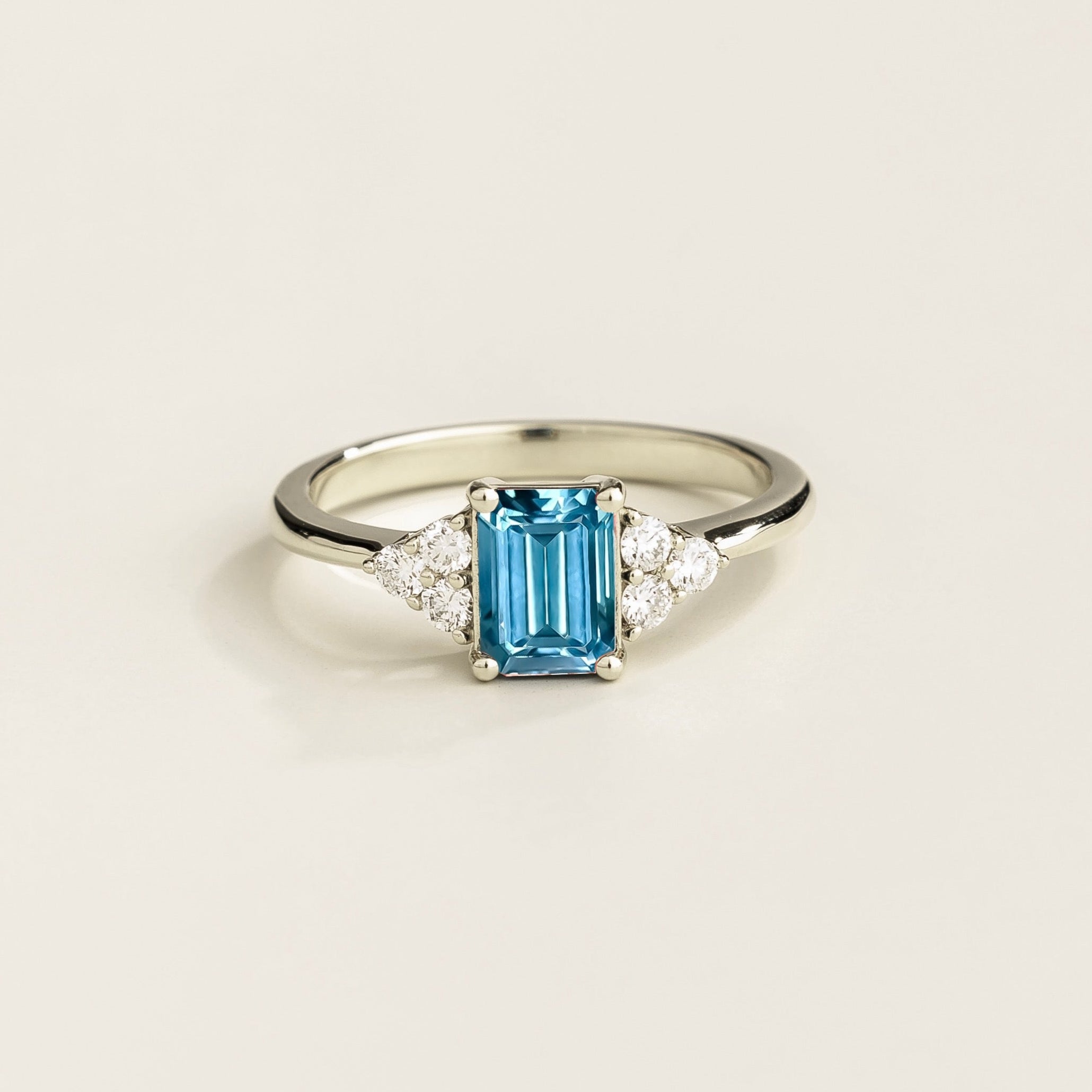 A white gold ring with an emerald-cut Aquamarine centerpiece and smaller Diamond accents on the sides.