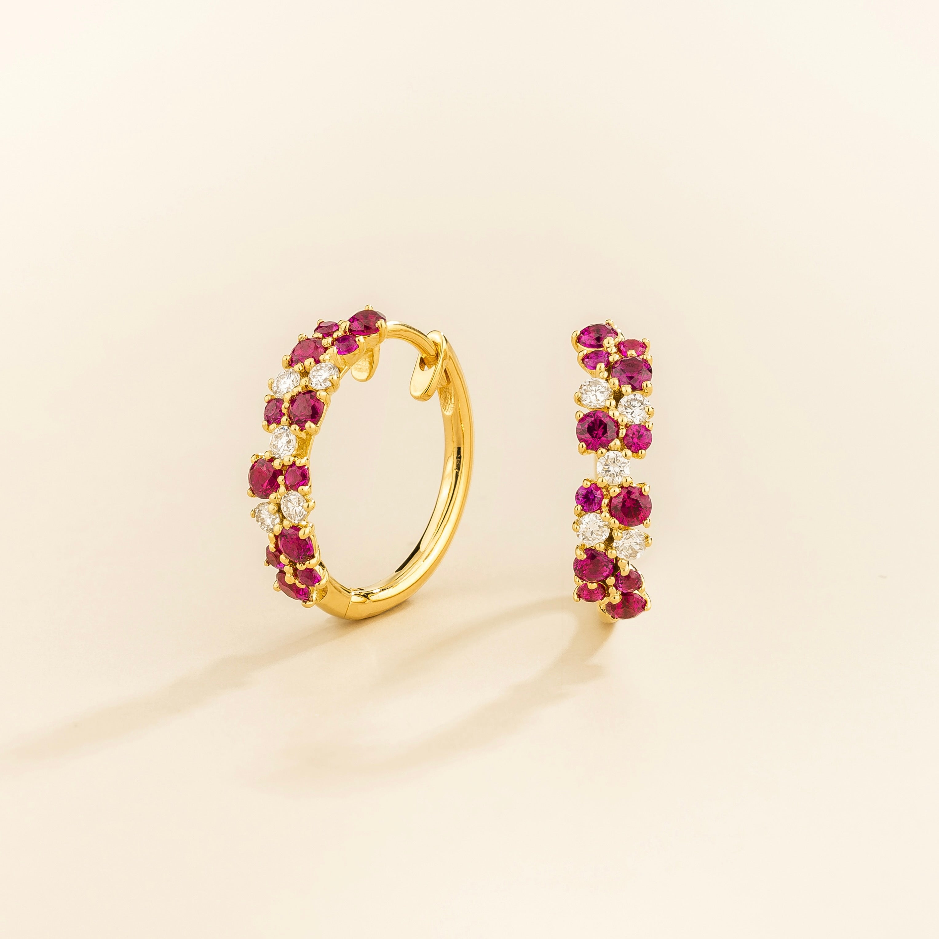 A pair of yellow gold huggie earrings set with cluster of round ruby and diamond accents, displayed against a neutral background.