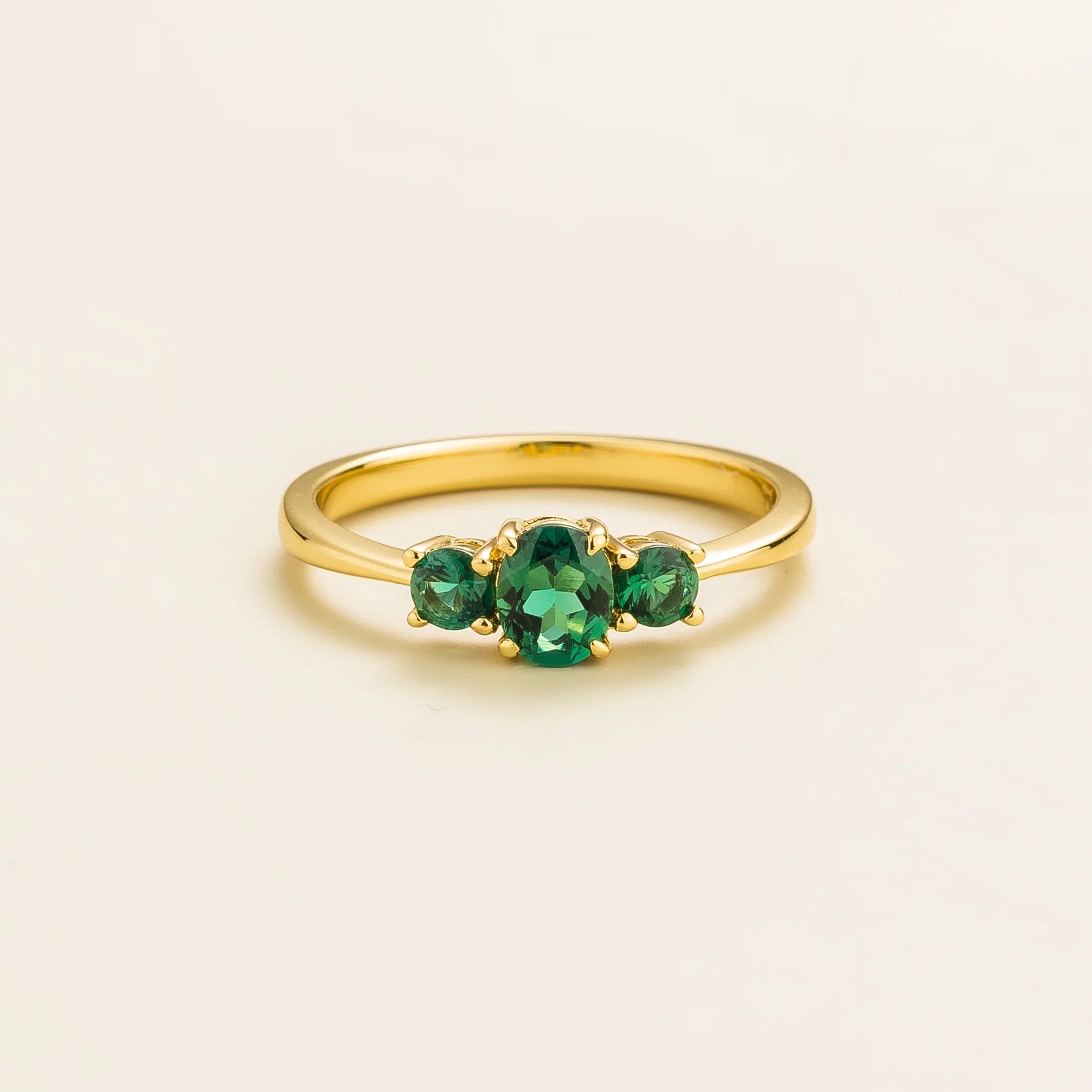 A gold ring featuring three green emerald gemstones set in a crown design.