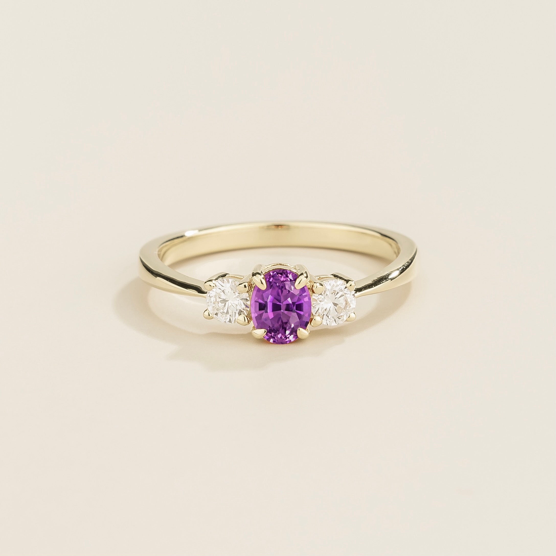 3 gemstones white gold ring with a purple sapphire center stone flanked by two diamond stones on a plain background.
