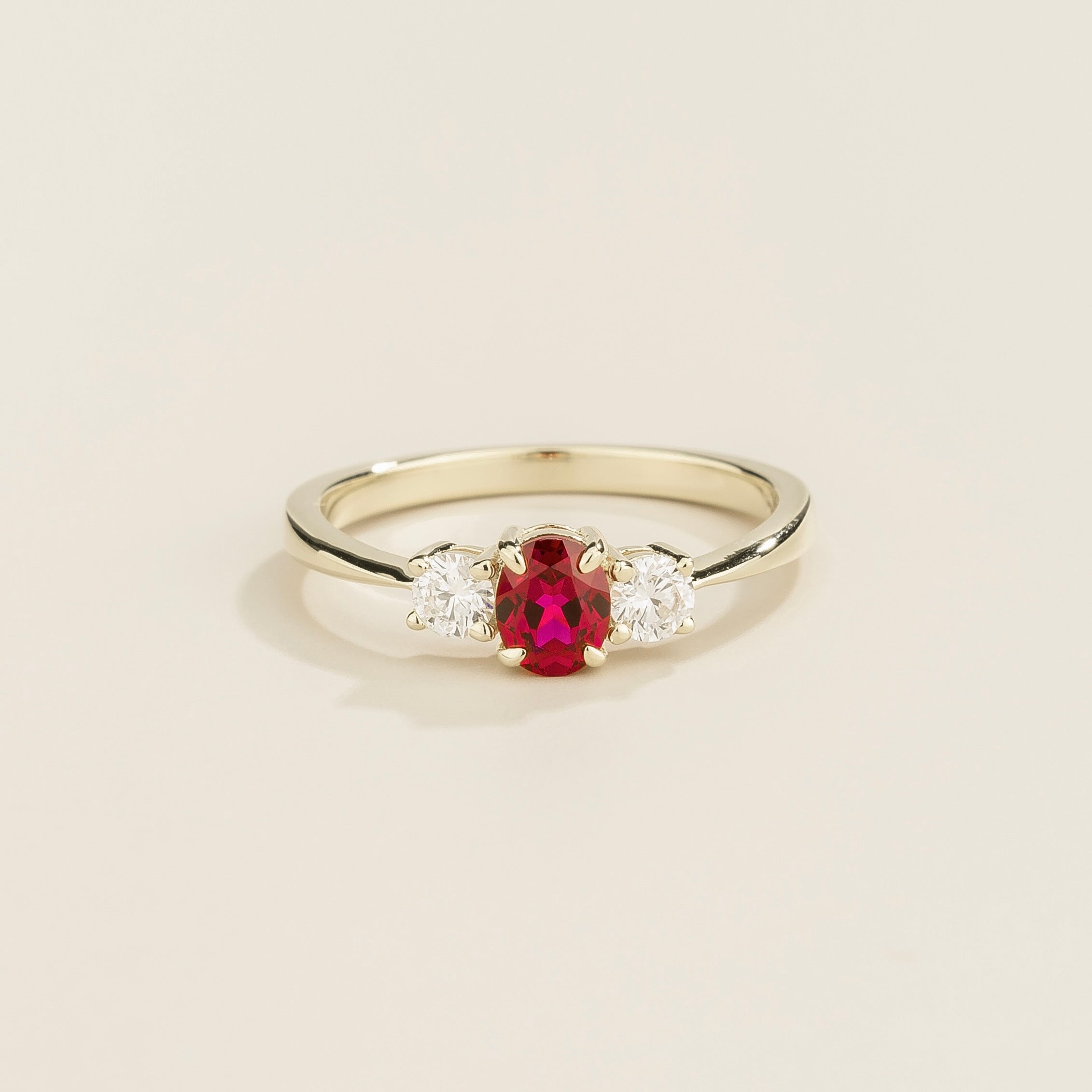 A white gold 3 gemstone ring set with a central ruby and flanked by two diamonds on either side, viewed from the front against a plain background.