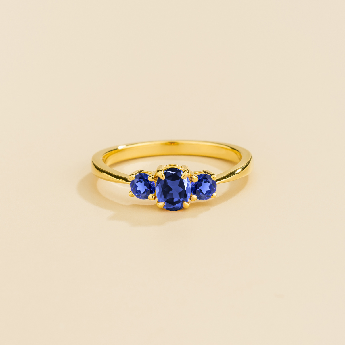 Gold ring with three royal blue sapphire gemstones on a beige background