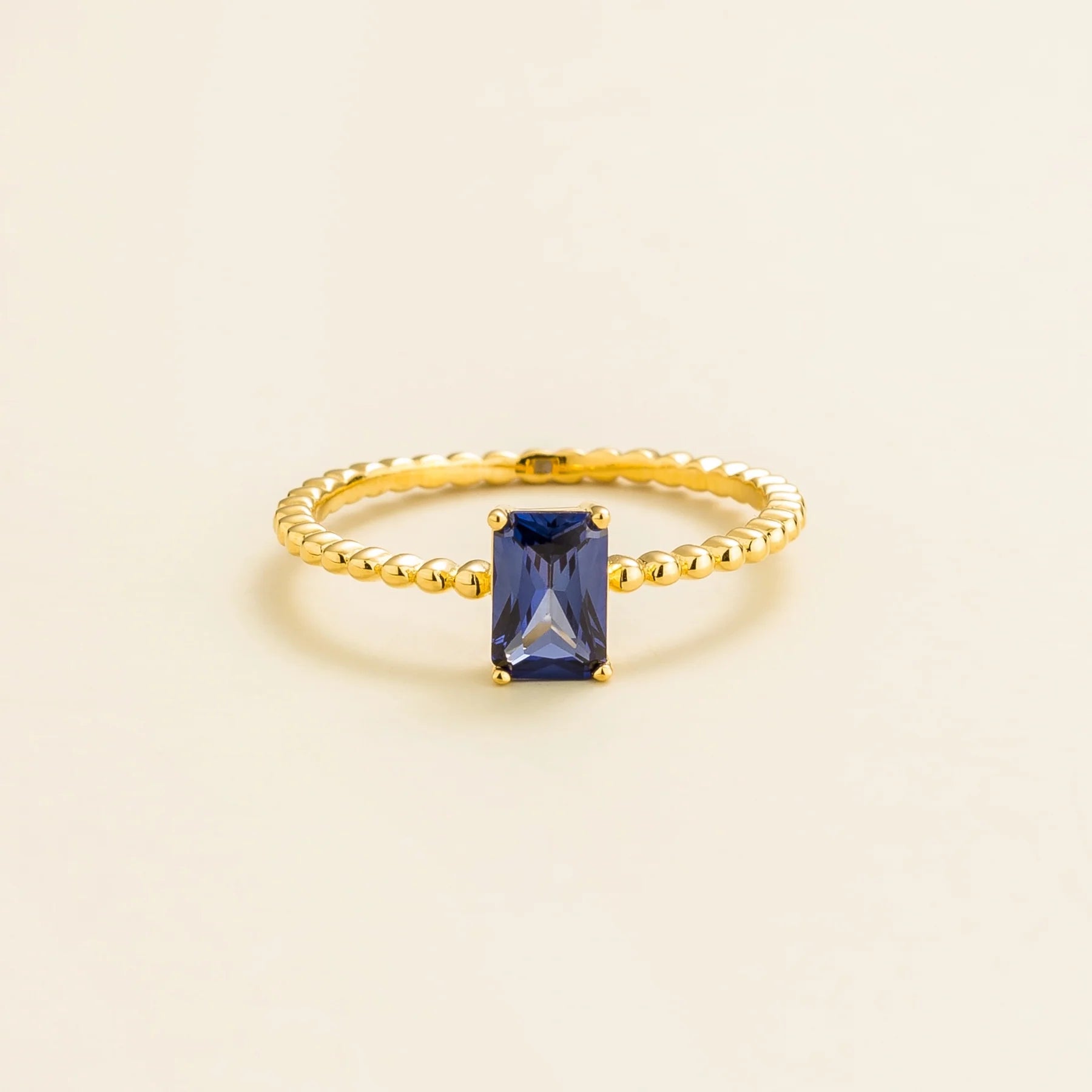 Juvetti gold ring featuring an emerald-cut lab-grown royal blue sapphire on a beaded band.