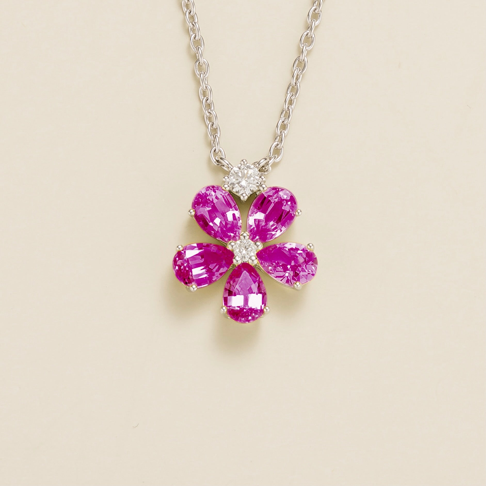 A white gold necklace with a floral pendant design, featuring vivid pink sapphires and smaller diamonds.