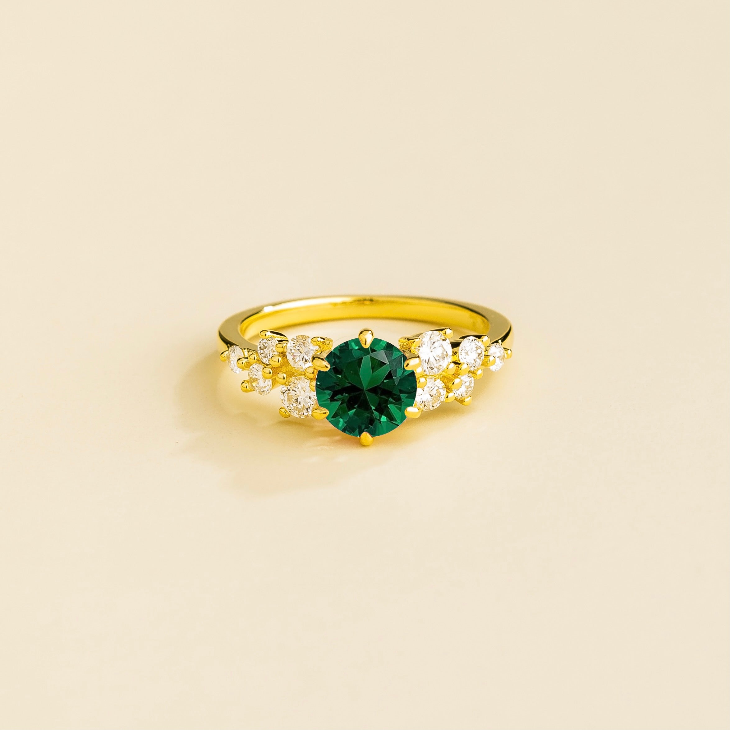 A gold ring with a emerald center stone and smaller diamonds cluster set in gold, displayed against a neutral background.