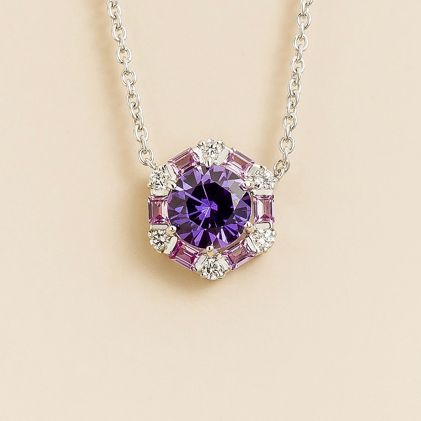 Hexagon necklace with round purple sapphire gemstone with pink sapphire and diamond halo on a beige background