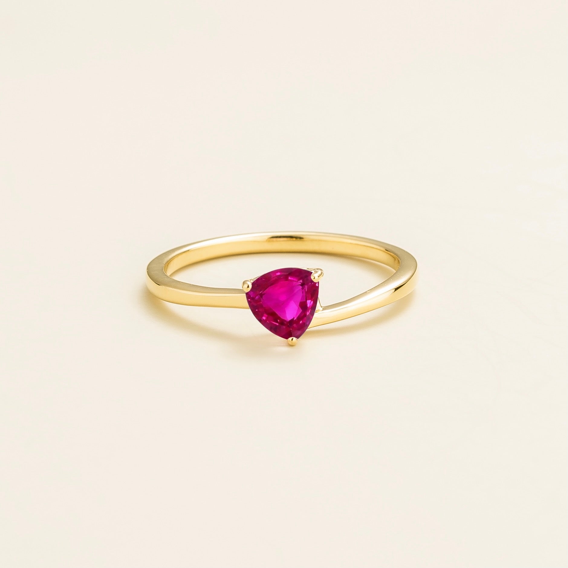 A solitaire gold ring with a trillion-cut vivid pink sapphire centerpiece set in a modern curved band.