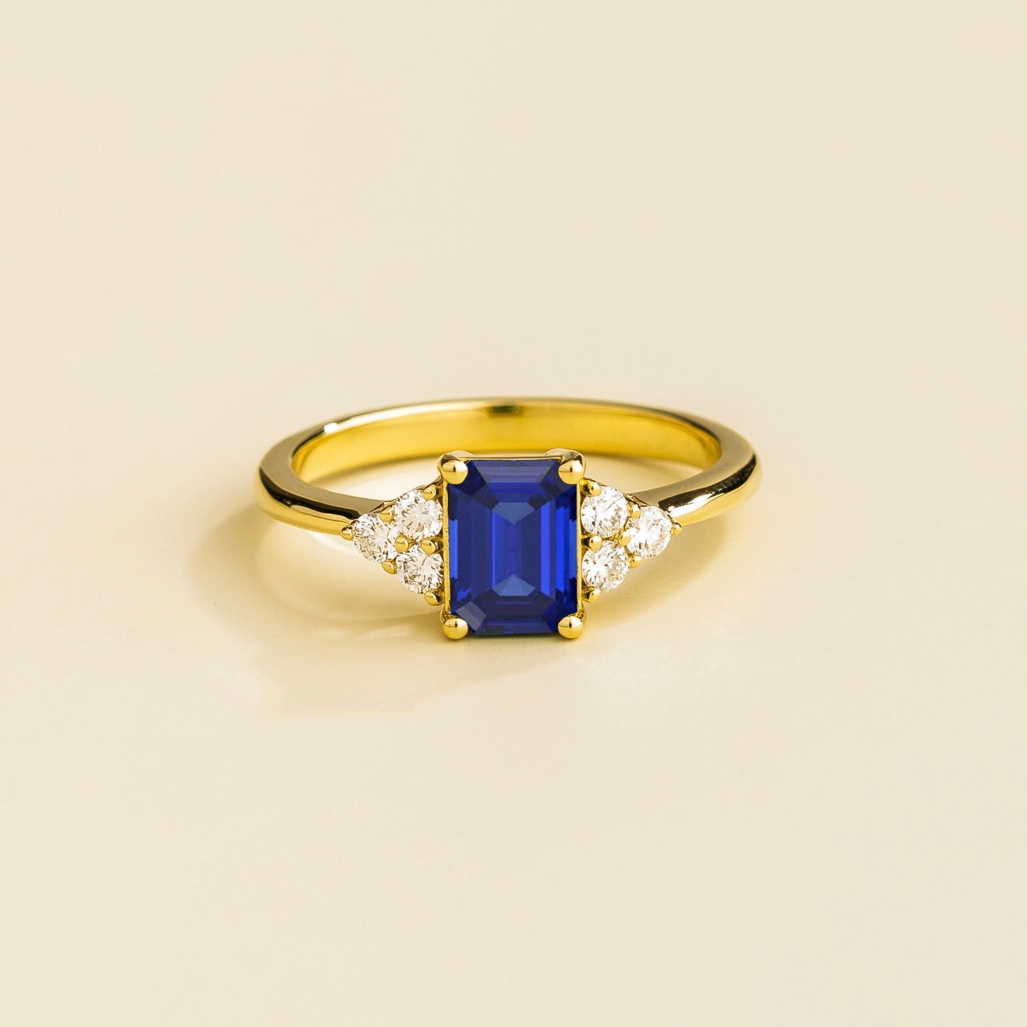 Juvetti yellow gold ring featuring an emerald-cut lab-grown royal blue sapphire with lab-grown diamond side stones.
