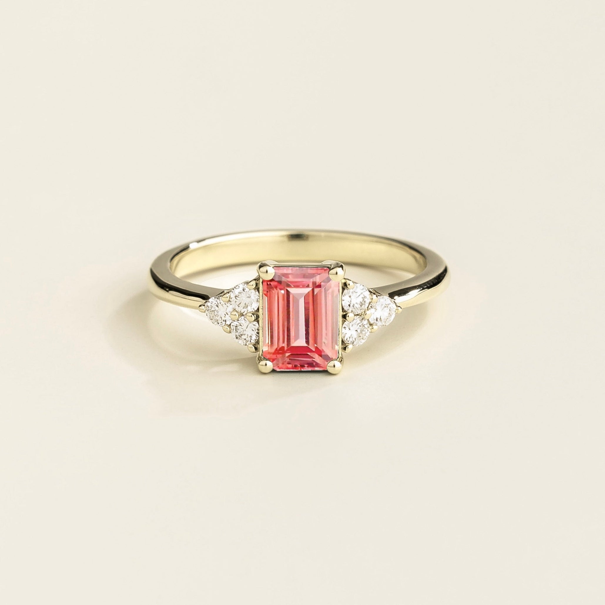A white gold ring with a Padparadscha Sapphire and Diamond, emerald cut, set in a ring with a gold band.