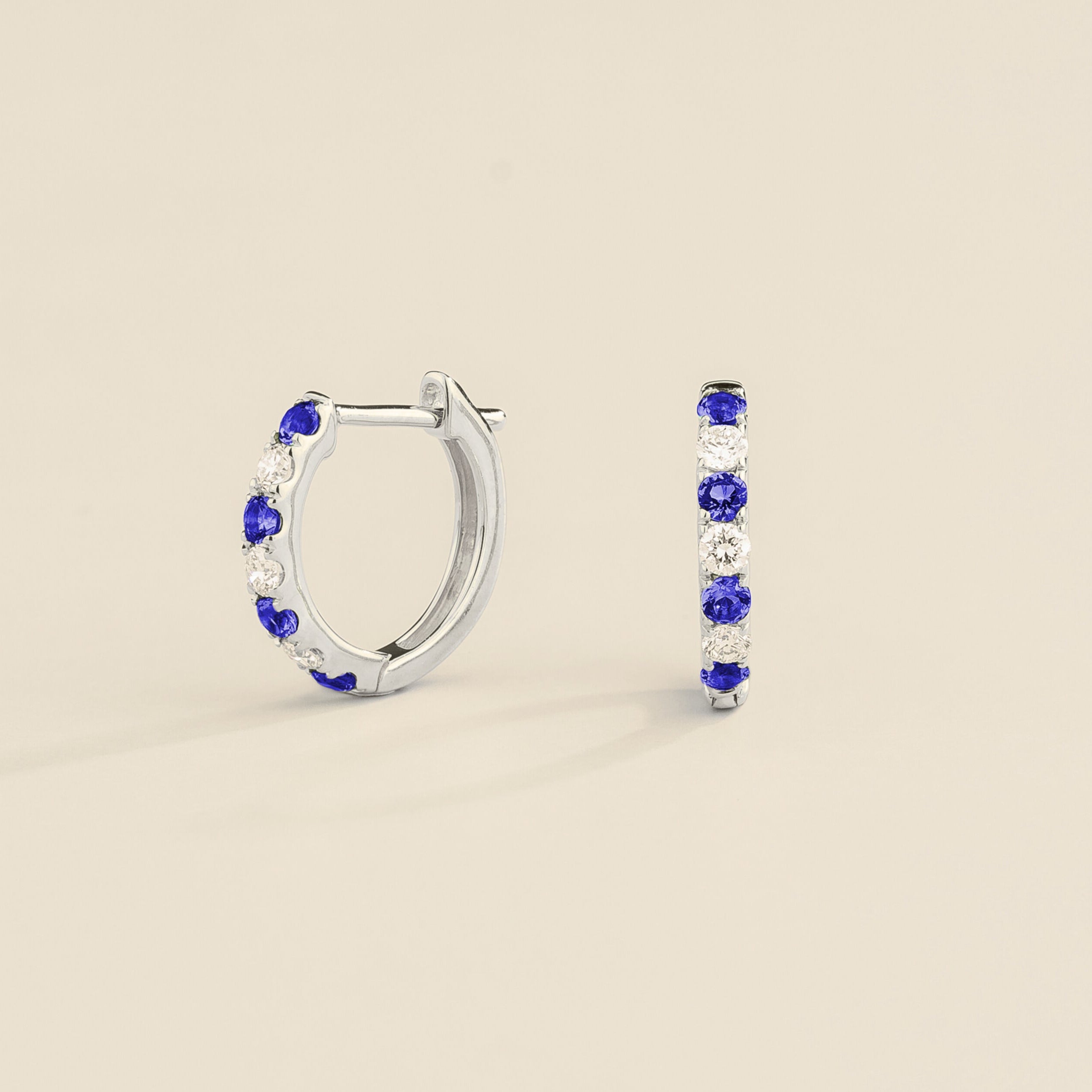 A pair of white gold huggie earrings set with blue sapphire and diamond accents.