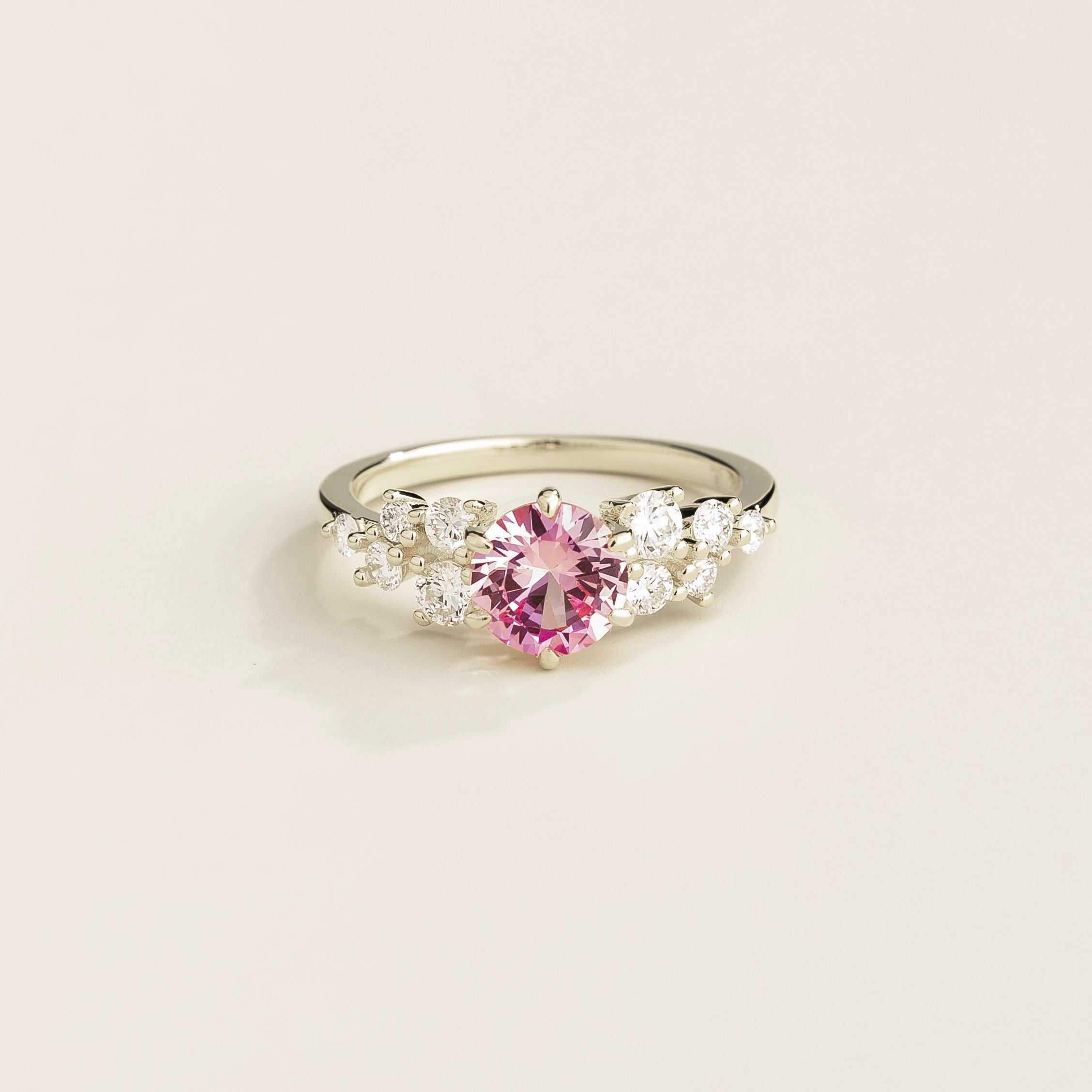 A white gold ring with a pink sapphire center stone and smaller diamonds cluster set in gold, displayed against a neutral background.
