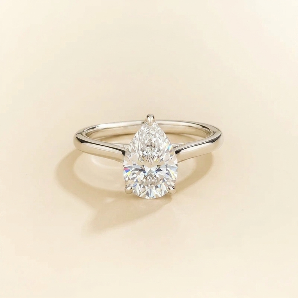 Solitaire engagement ring with a 2 carat pear-cut diamond in a three-prong cathedral setting on a slim polished white-metal band.