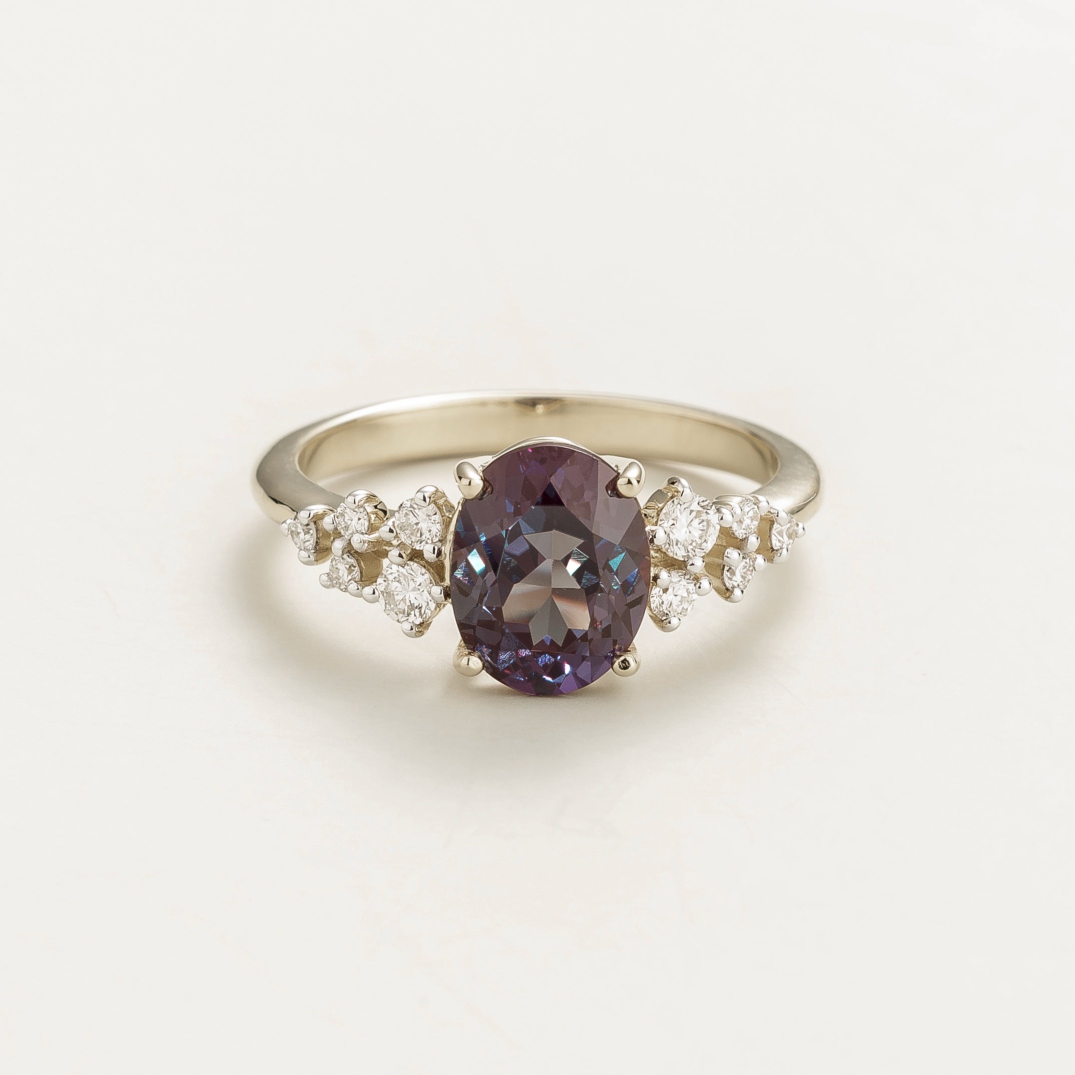 A white gold ring with a central oval alexandrite gemstone and smaller diamonds cluster