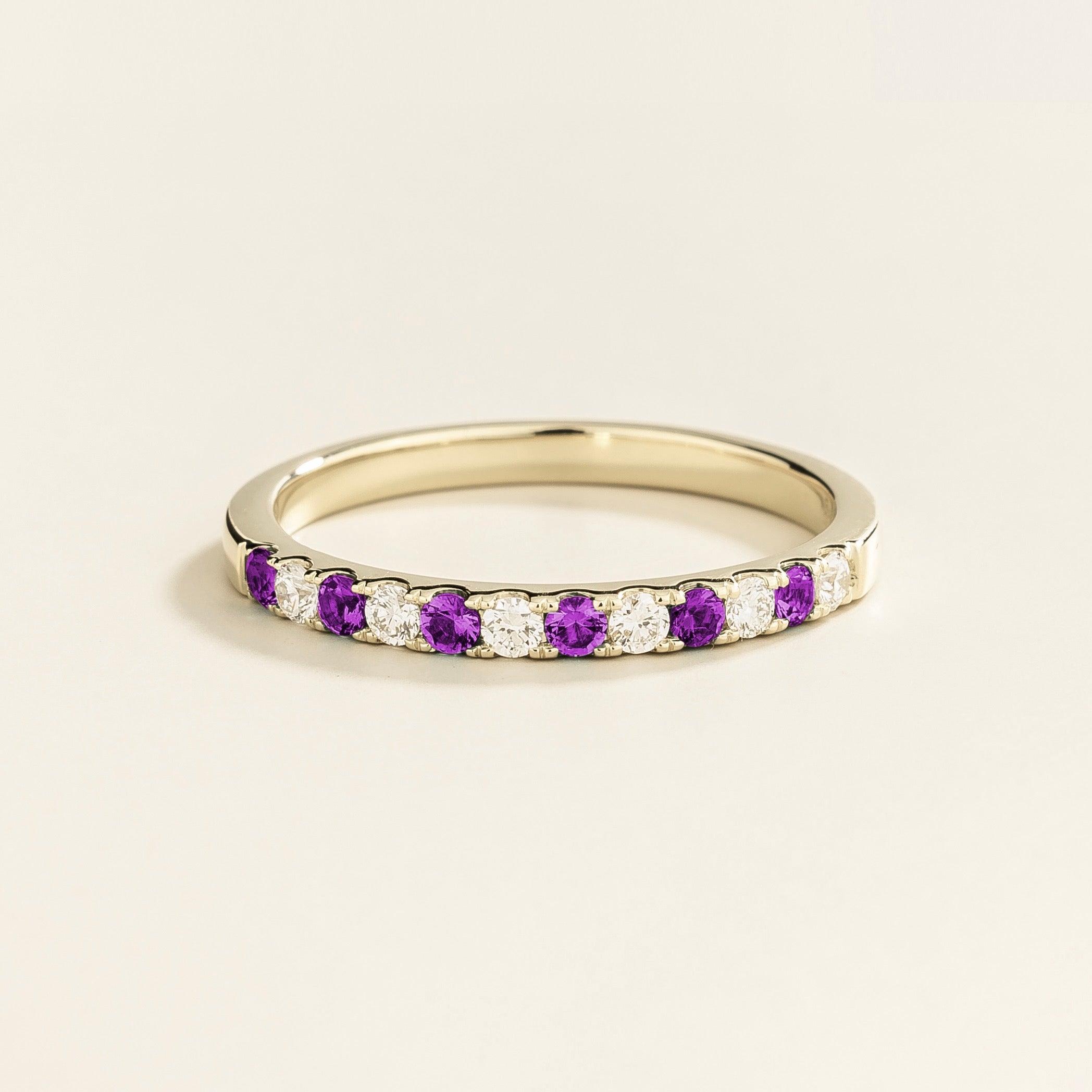 A white gold half eternity ring with alternating purple sapphire and diamond elements.