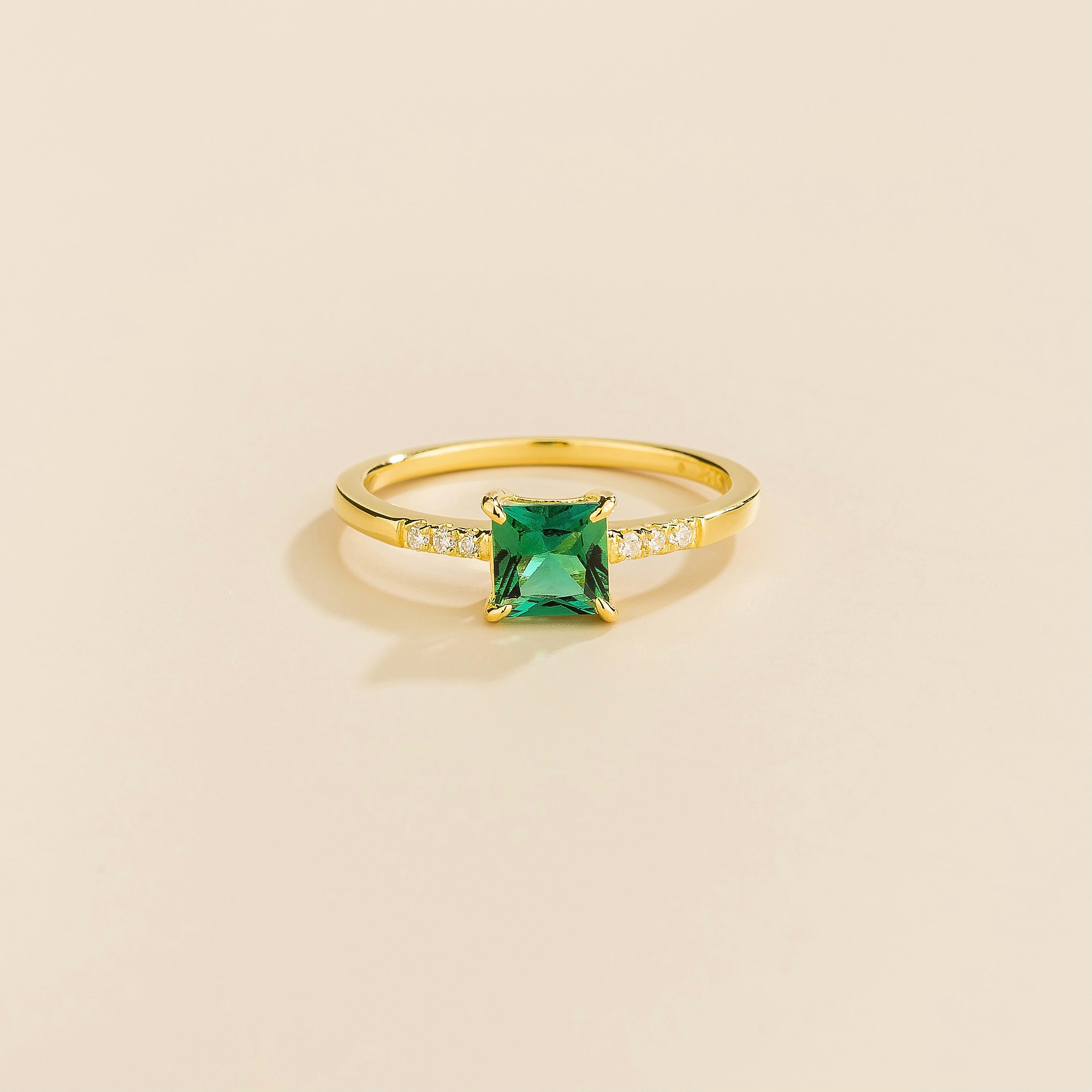 Juvetti yellow gold ring featuring a princess-cut lab-grown emerald with diamond side stones.