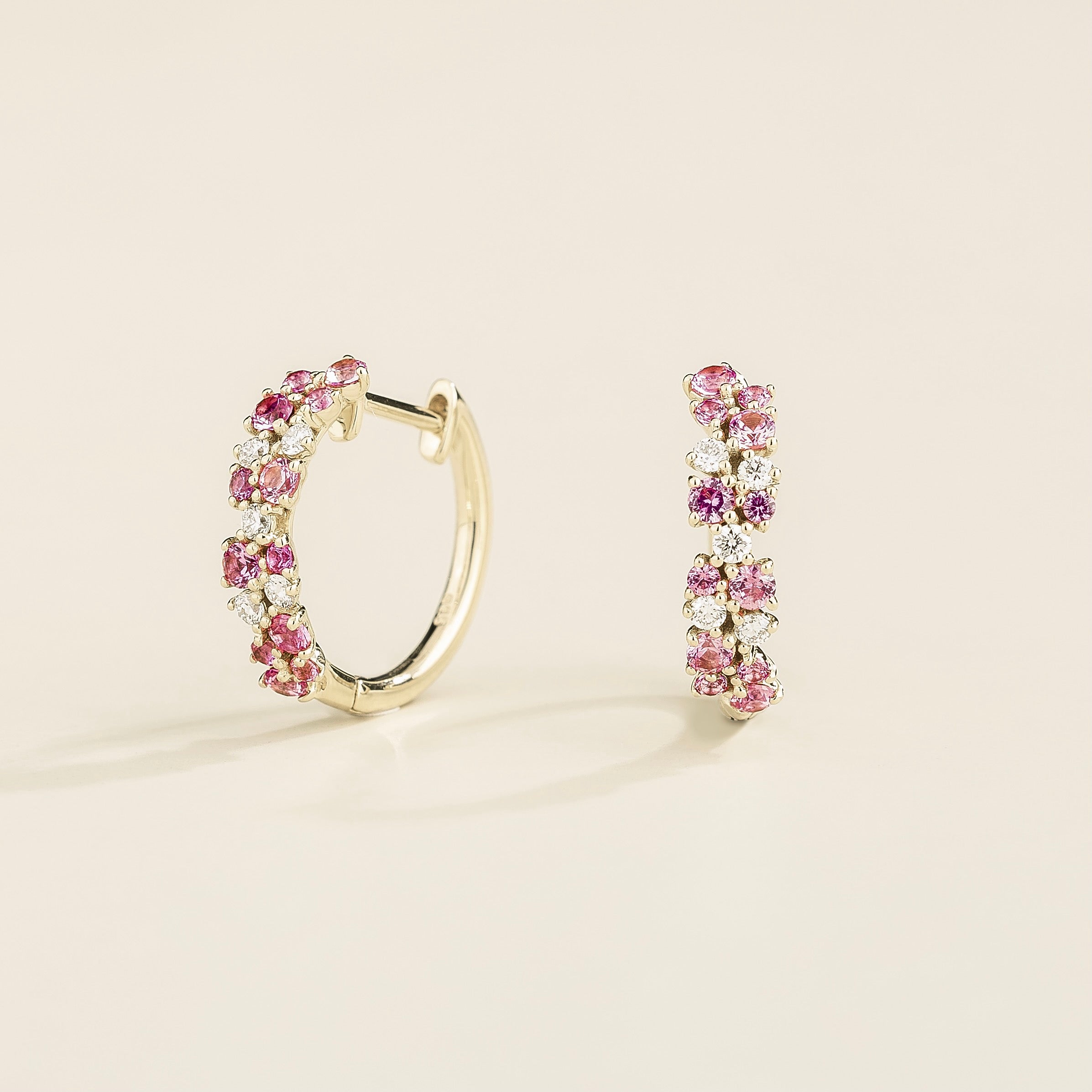 A pair of white gold huggie earrings set with cluster of round pink sapphire and diamond accents, displayed against a neutral background.