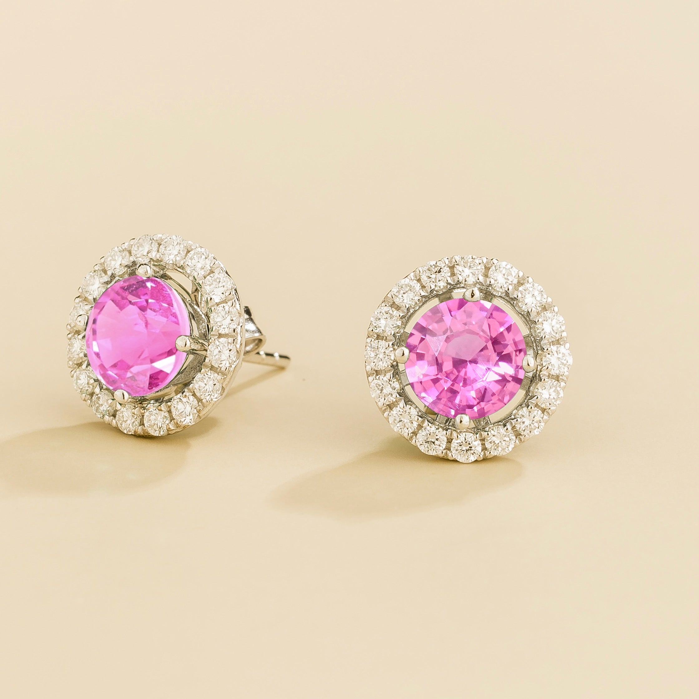 A pair of white gold floret earrings set with a round pink sapphire centerpiece and surrounding round diamonds halo. Removable halo piece.