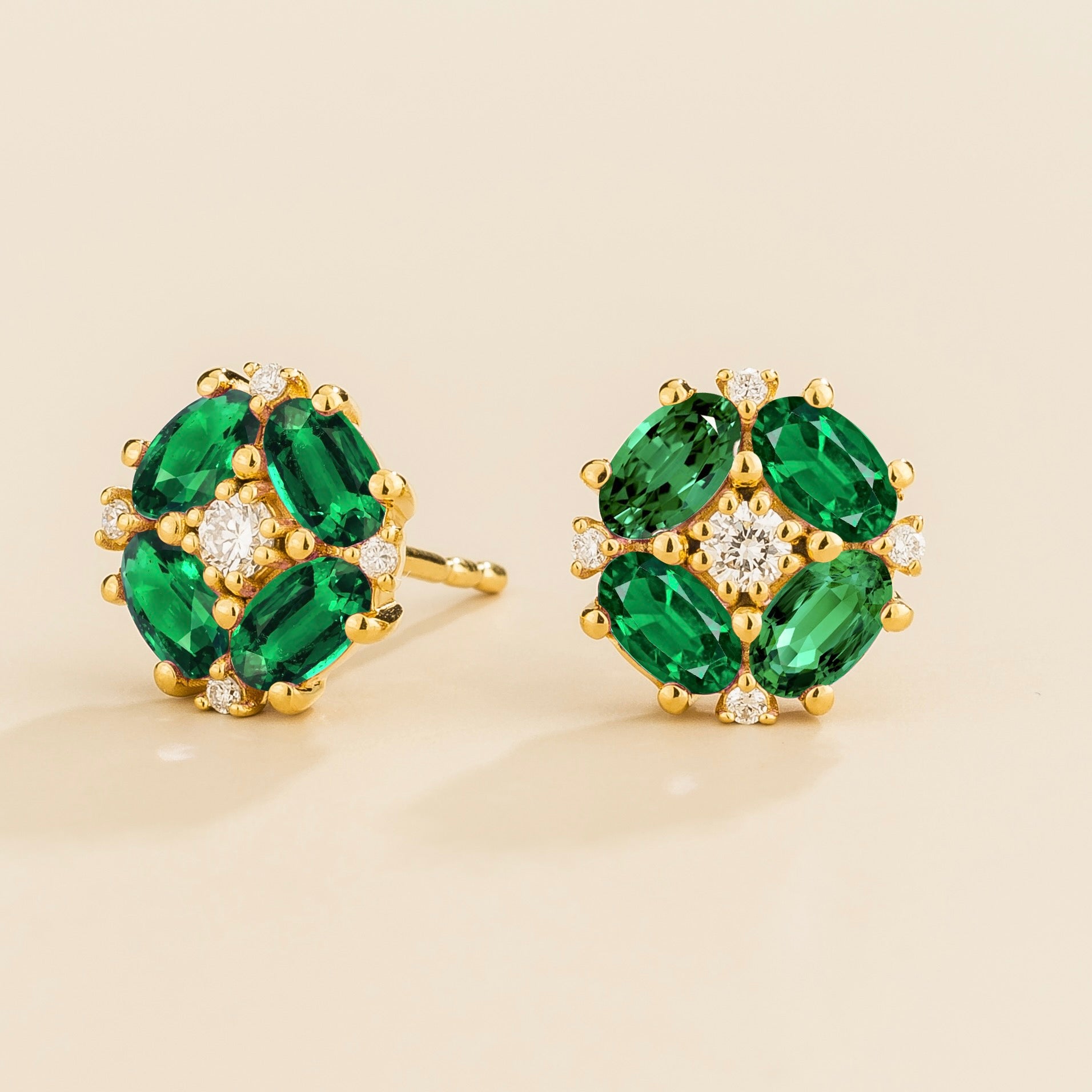 A pair of gold earrings featuring oval green emeralds and round diamonds arranged in a floral pattern.