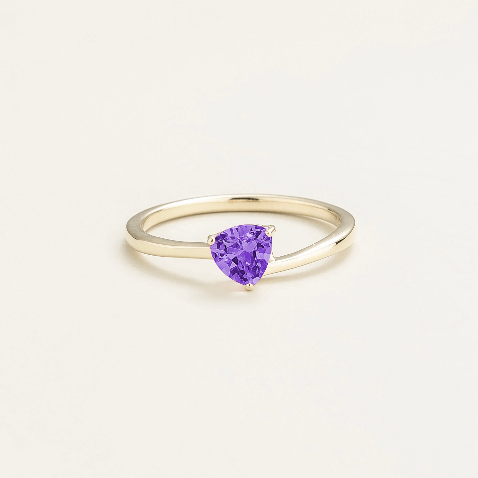 A solitaire white gold ring with a trillion-cut purple sapphire centerpiece set in a modern curved band.