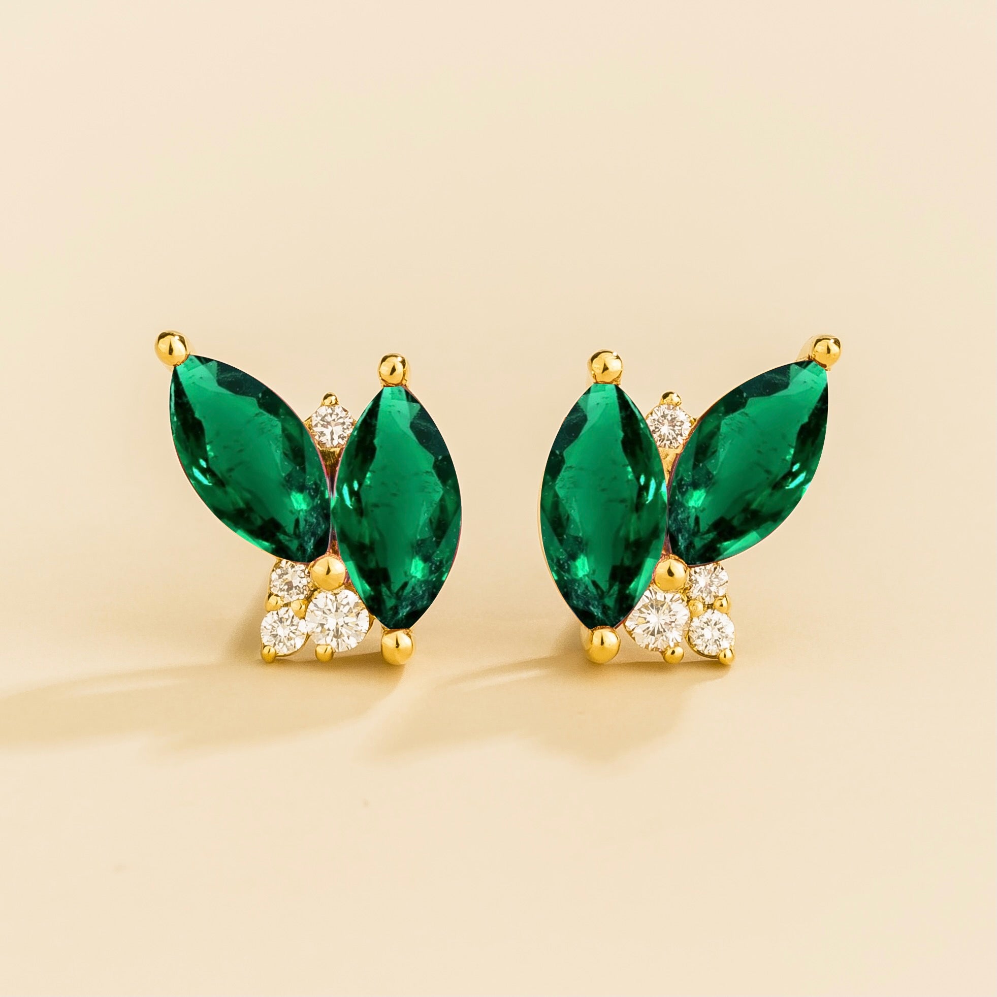 A pair of Vento gold earrings featuring marquis emeralds and round diamonds, with a butterfly-like shape and a yellow gold setting.