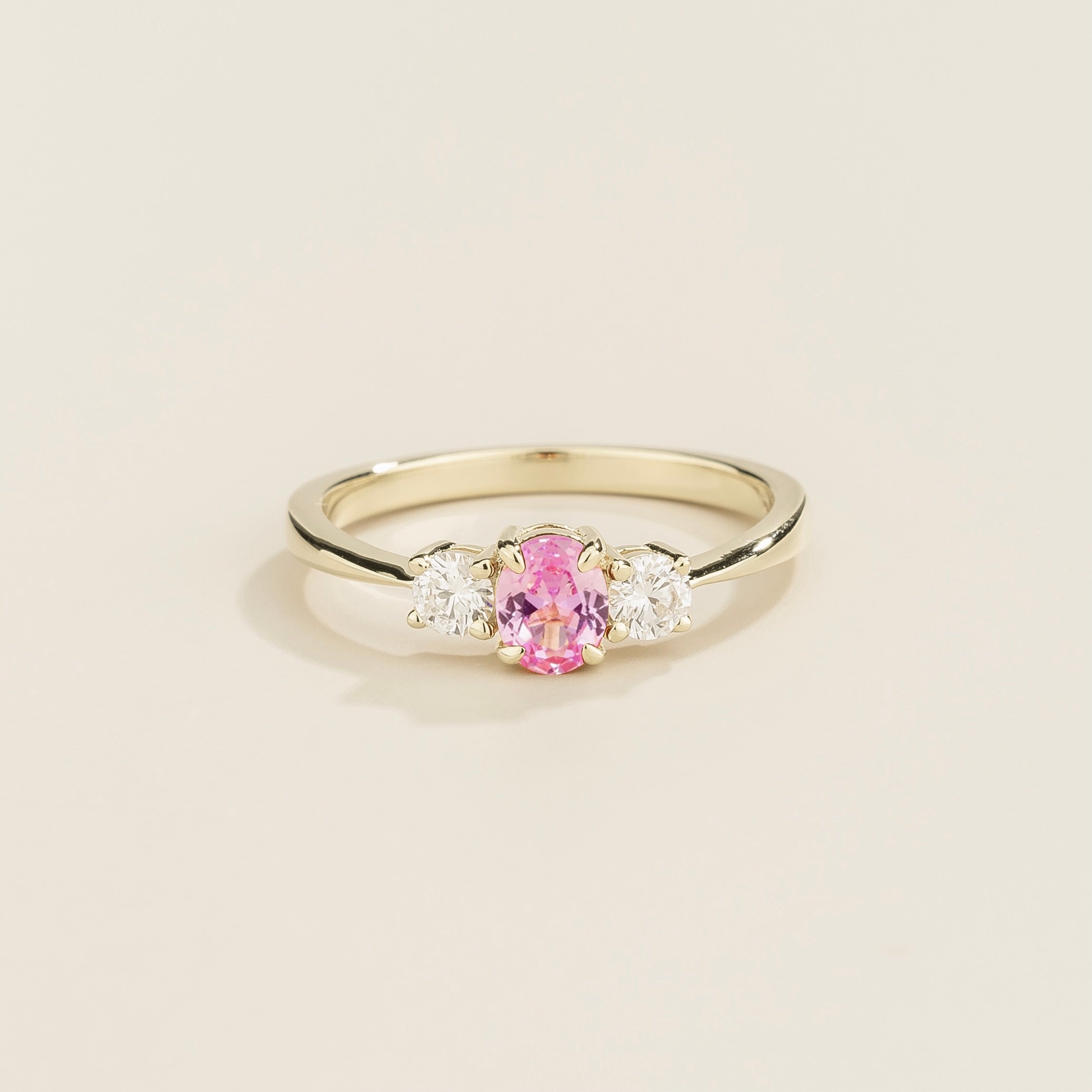 A white gold ring with a central pink sapphire gem surrounded by two smaller diamond gems on each side.