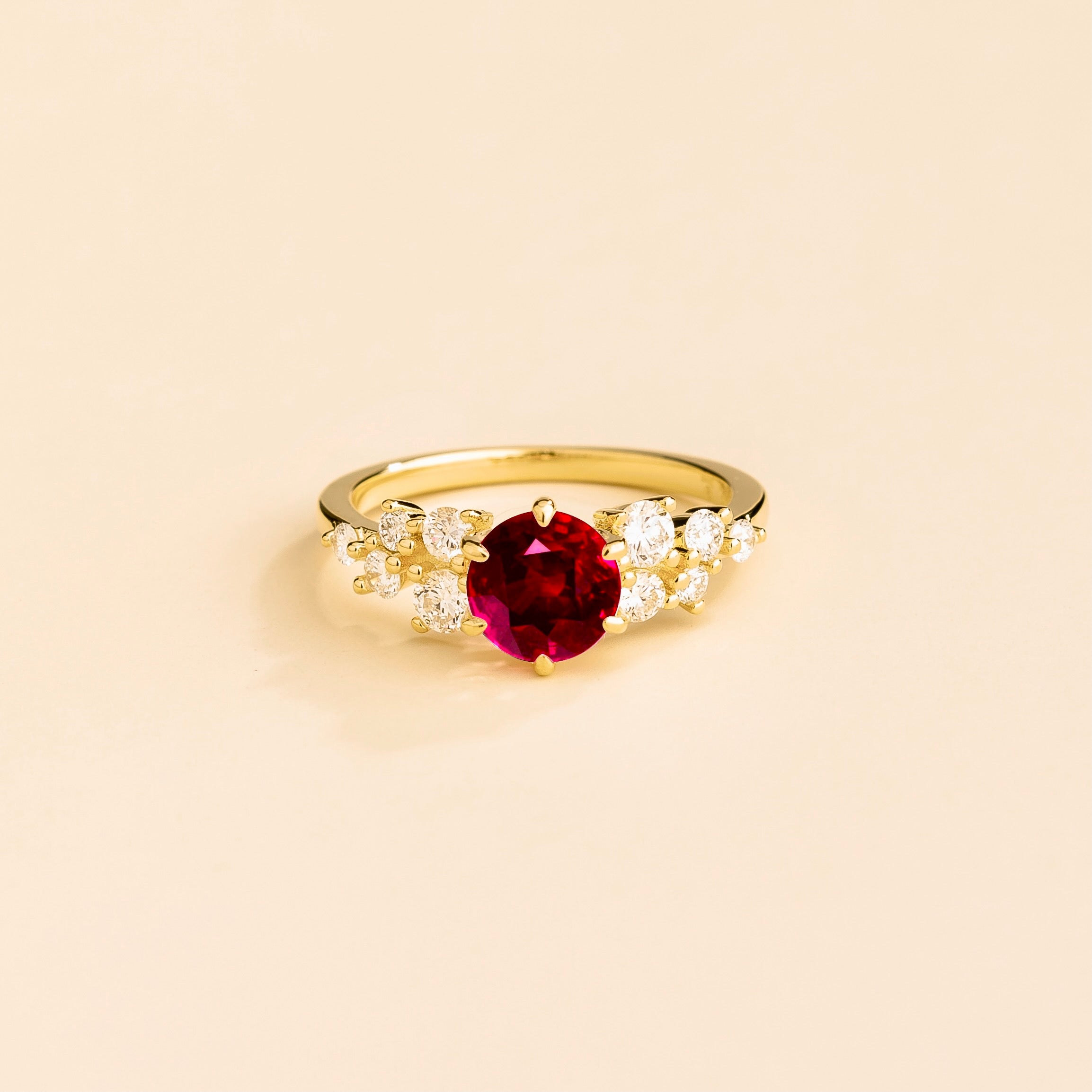 A gold ring with a ruby center stone and smaller diamonds cluster set in gold, displayed against a neutral background.