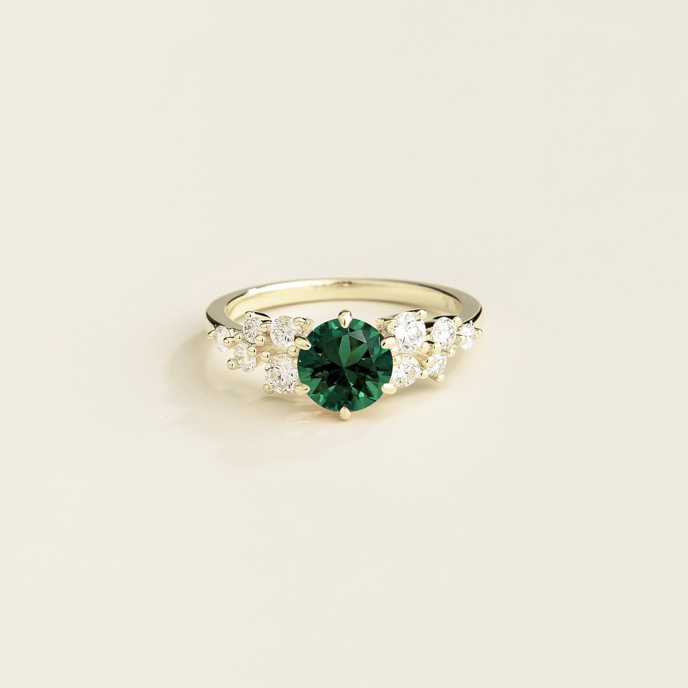 A white gold ring with a emerald center stone and smaller diamonds cluster set in gold, displayed against a neutral background.