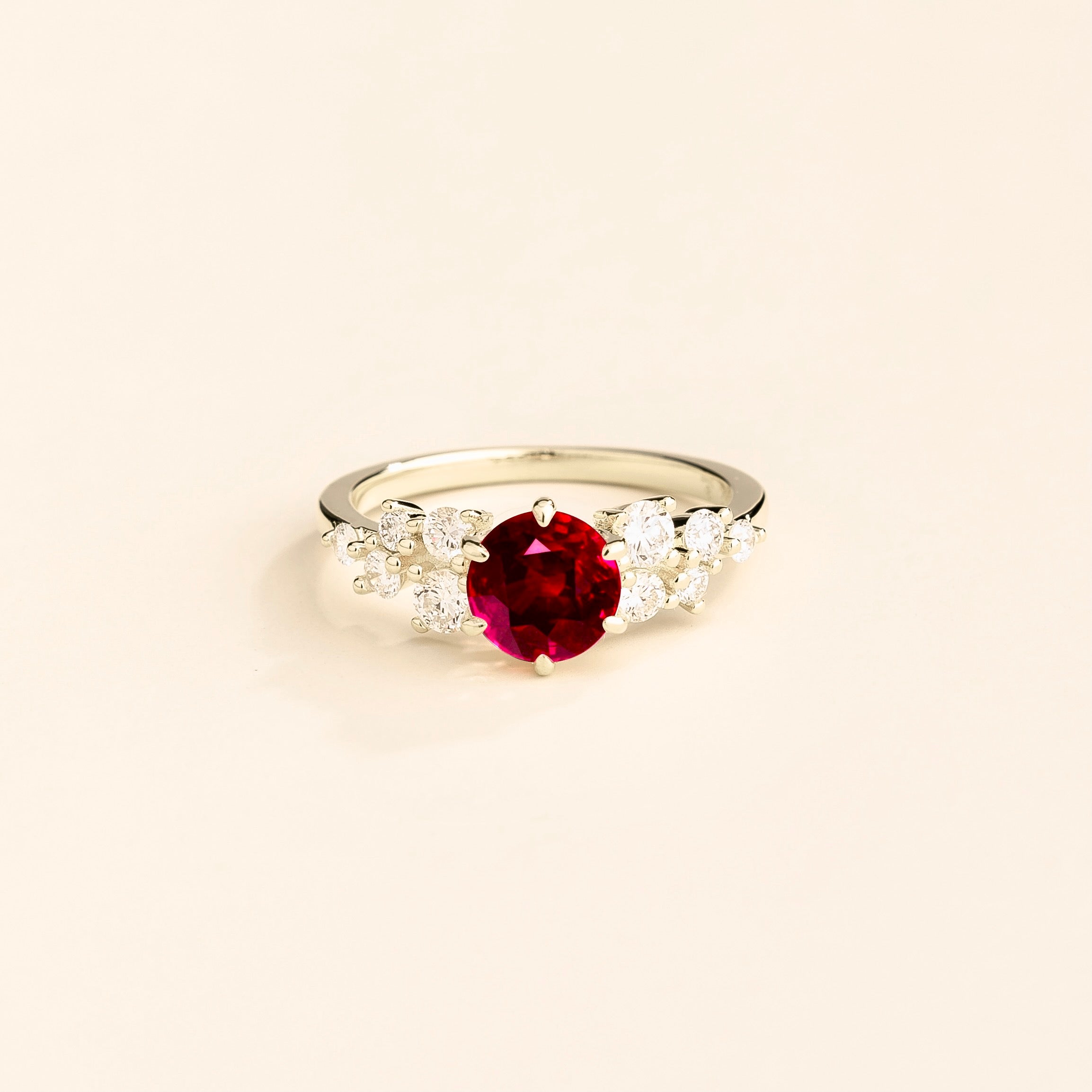 A white gold ring with a ruby center stone and smaller diamonds cluster set in gold, displayed against a neutral background.