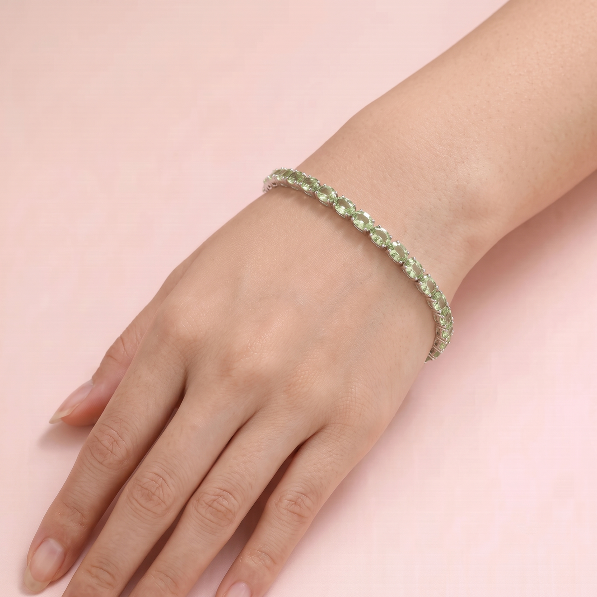 A model is wearing white gold tennis bracelet set with oval green sapphire gemstones.