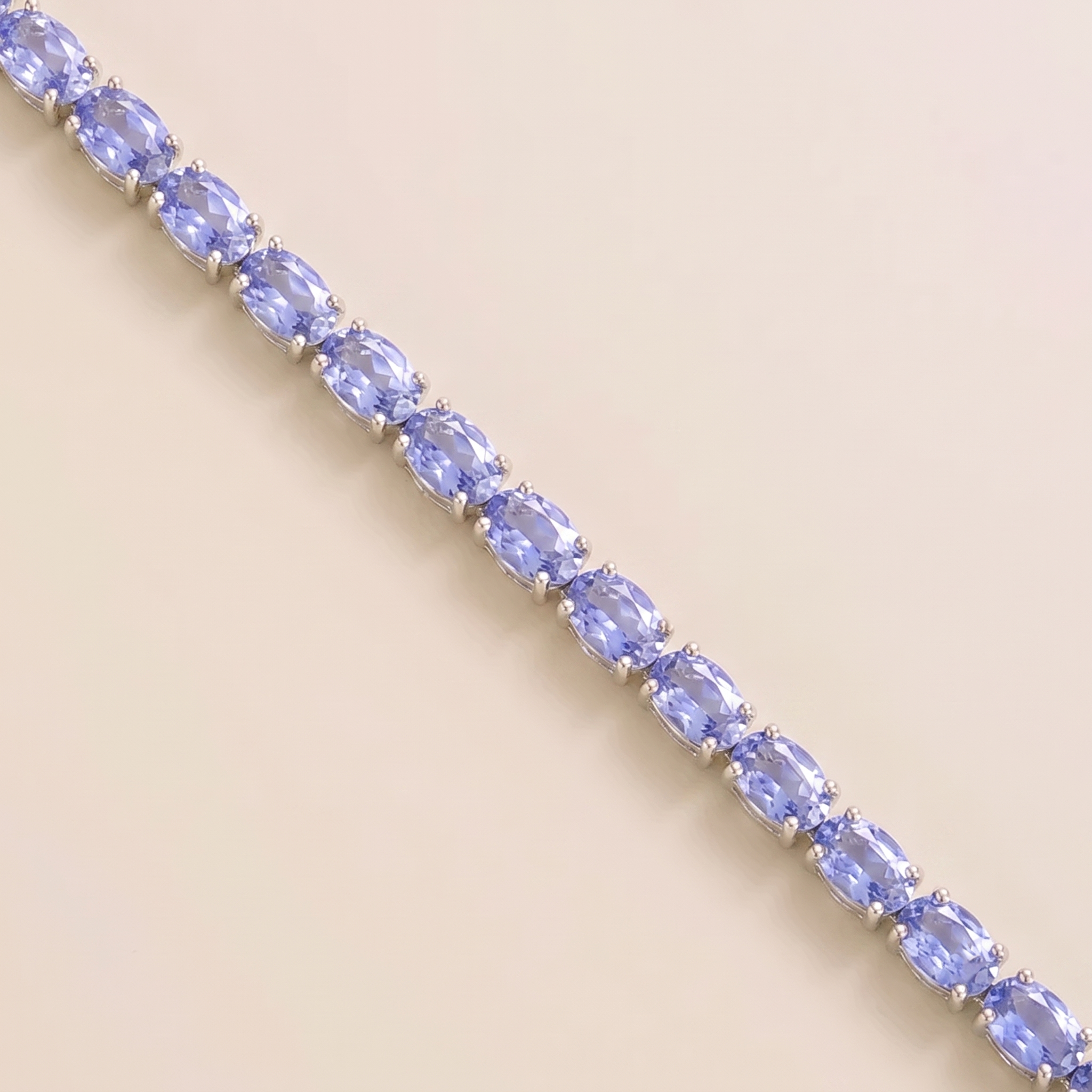 A white gold tennis bracelet set with oval light blue sapphire gemstones.