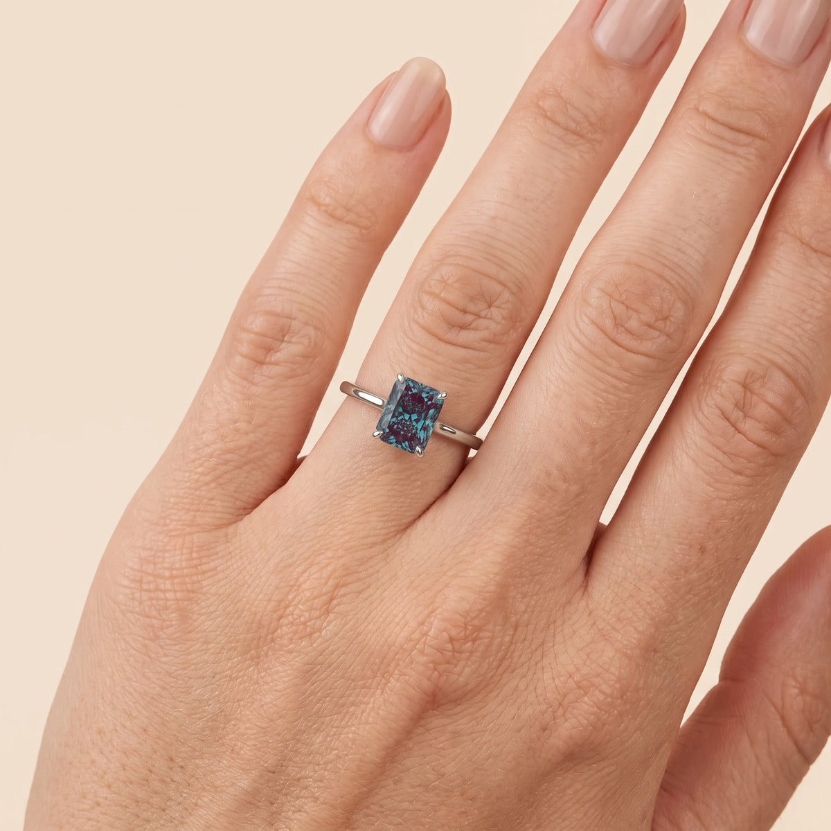 A model is wearing The Clair Radiant Shape Alexandrite Cathedral Solitaire Ring