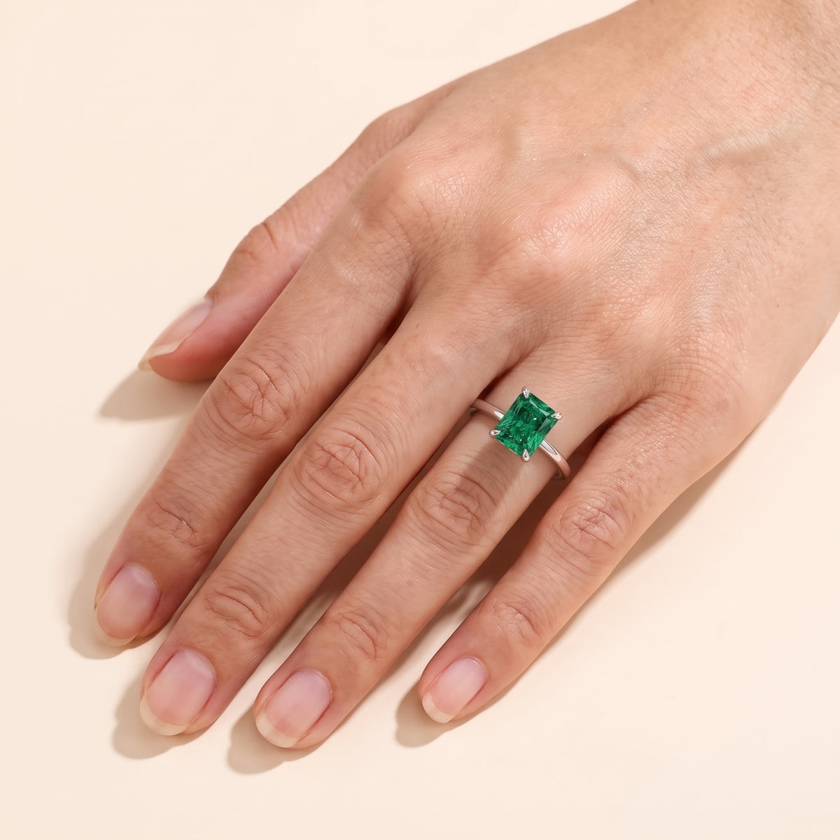 A model is wearing The Clair Radiant Shape Emerald Cathedral Solitaire Ring