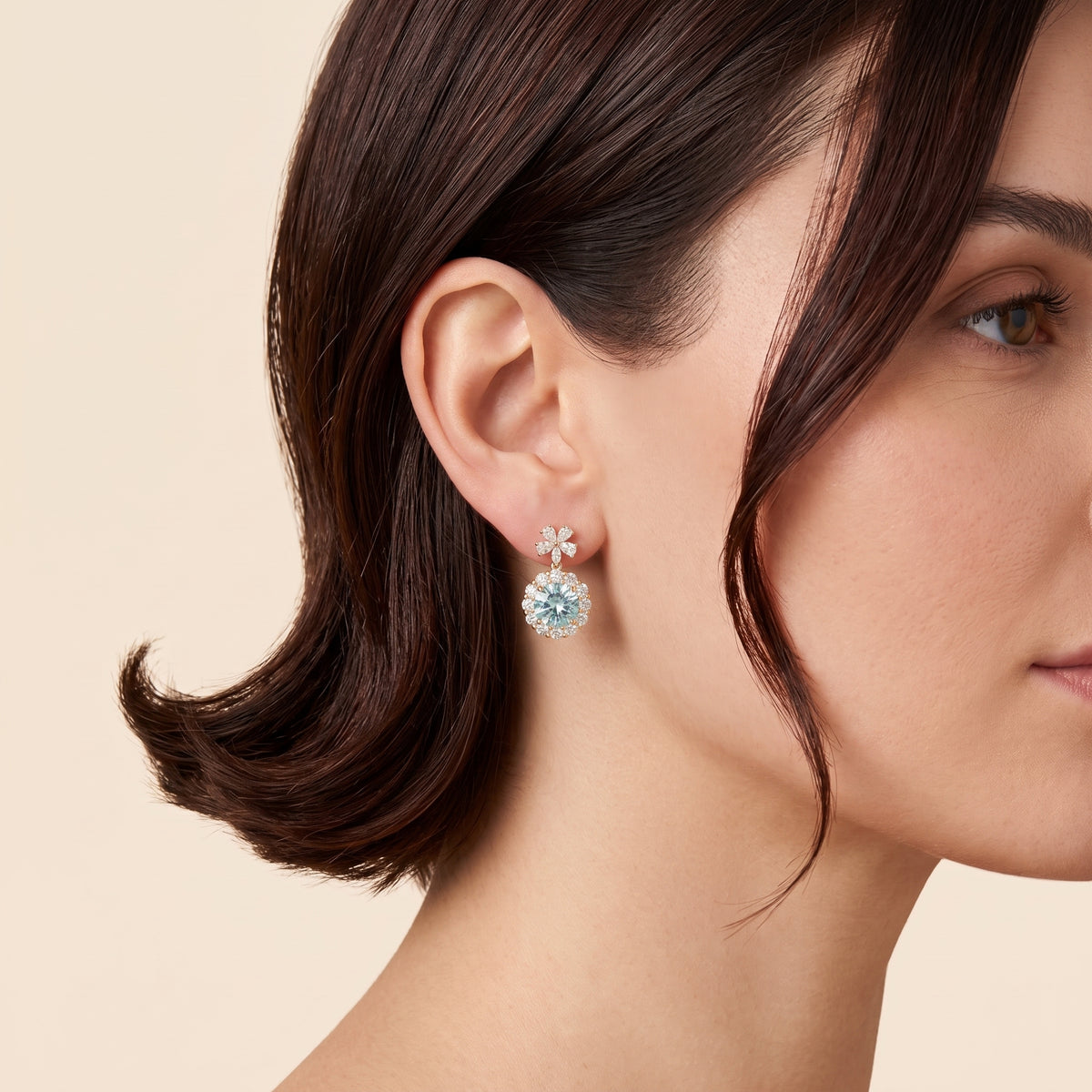 A model is wearing The Antoinette Round Aquamarine & Diamond Halo Pendant Earrings with Flower Bail