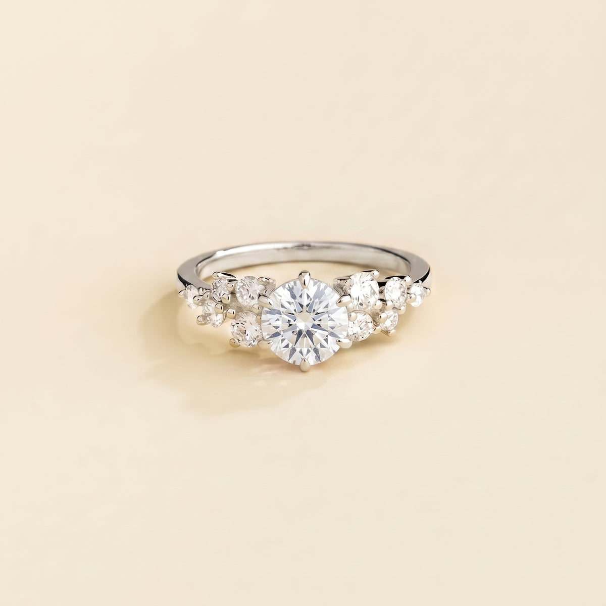 A white gold ring with a diamond center stone and smaller diamonds cluster set in white gold, displayed against a neutral background.