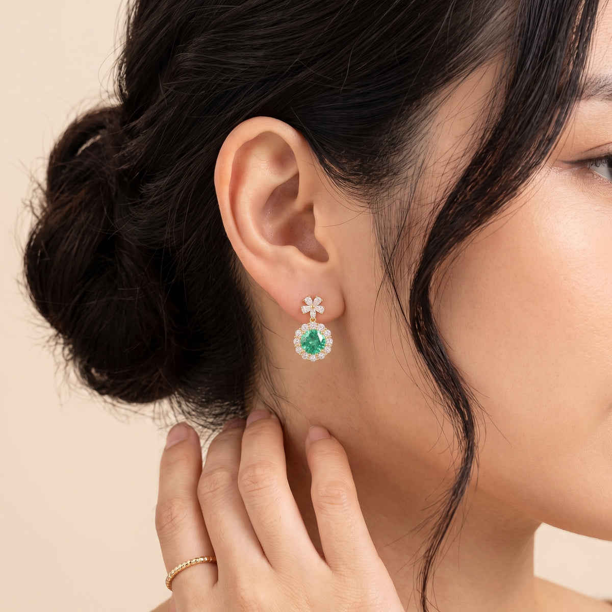 A model is wearing The Antoinette Round Green Sapphire & Diamond Halo Pendant Earrings with Flower Bail