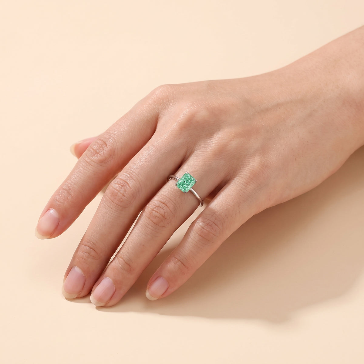 A model is wearing The Clair Radiant Shape Green Sapphire Cathedral Solitaire Ring