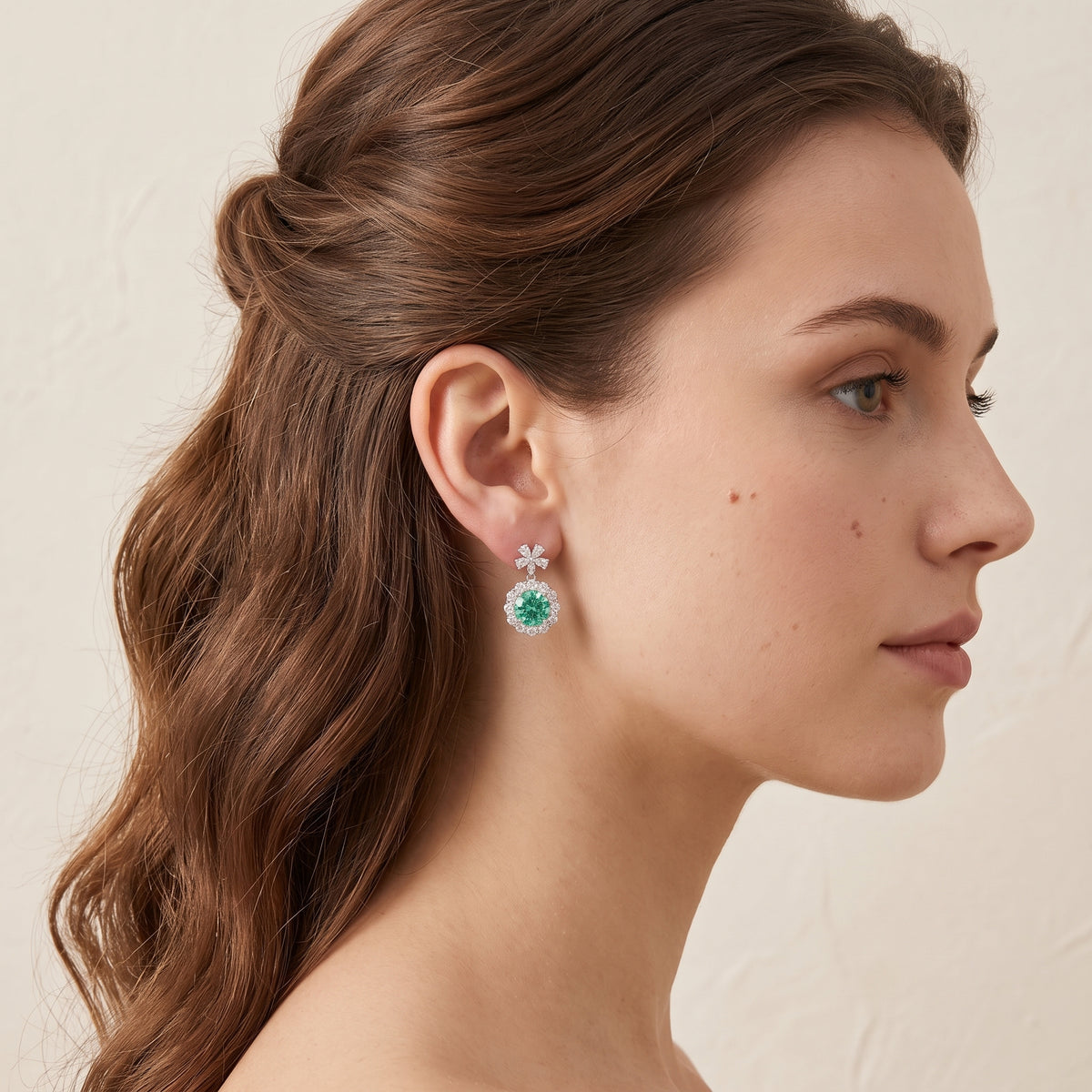 A model is wearing The Antoinette Round Green Sapphire & Diamond Halo Pendant Earrings with Flower Bail